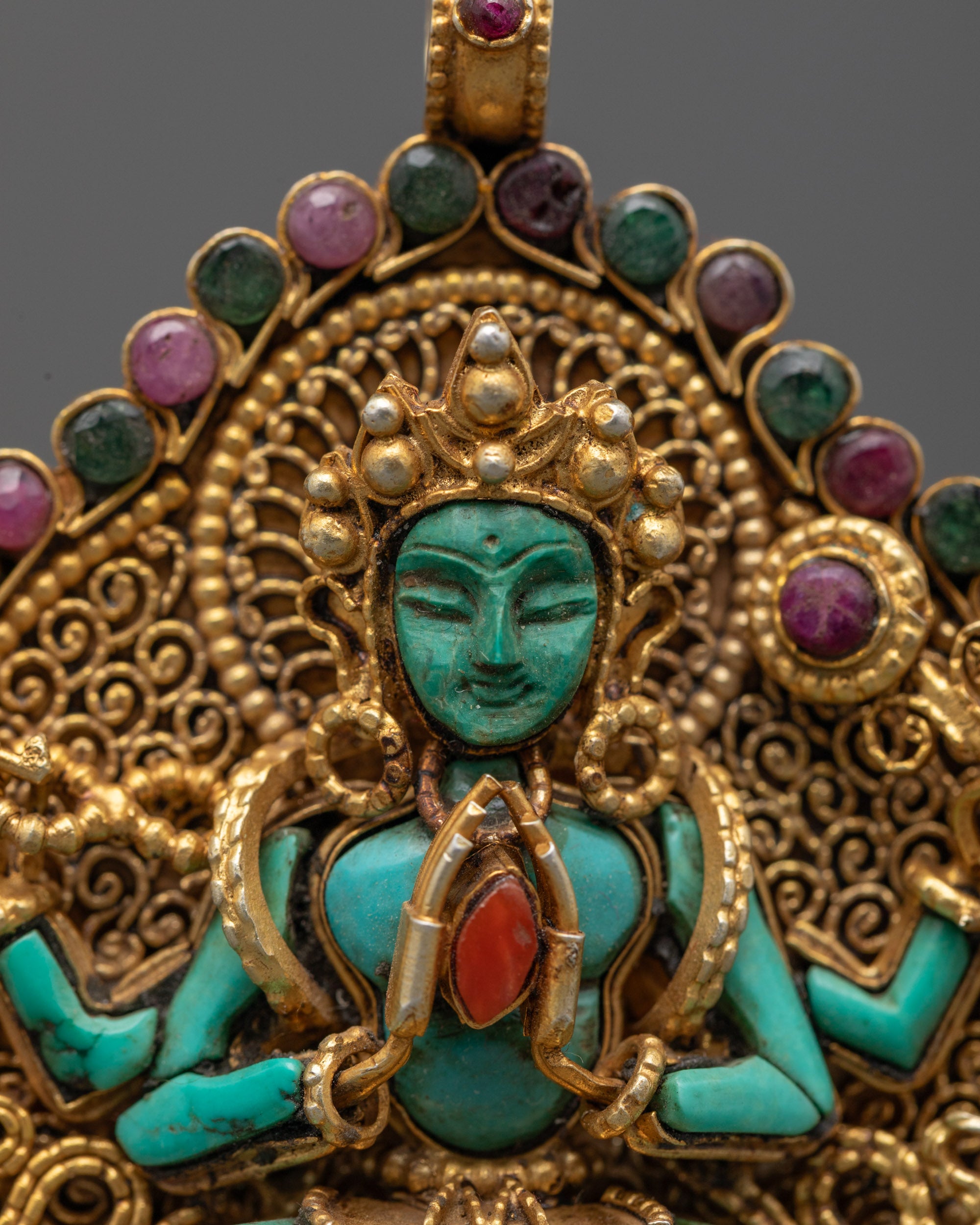 Close-up of green crystal Chenrezig clutching coral wish-fulfilling gem on gold-gilded filigree locket, handcrafted in Patan, Nepal.