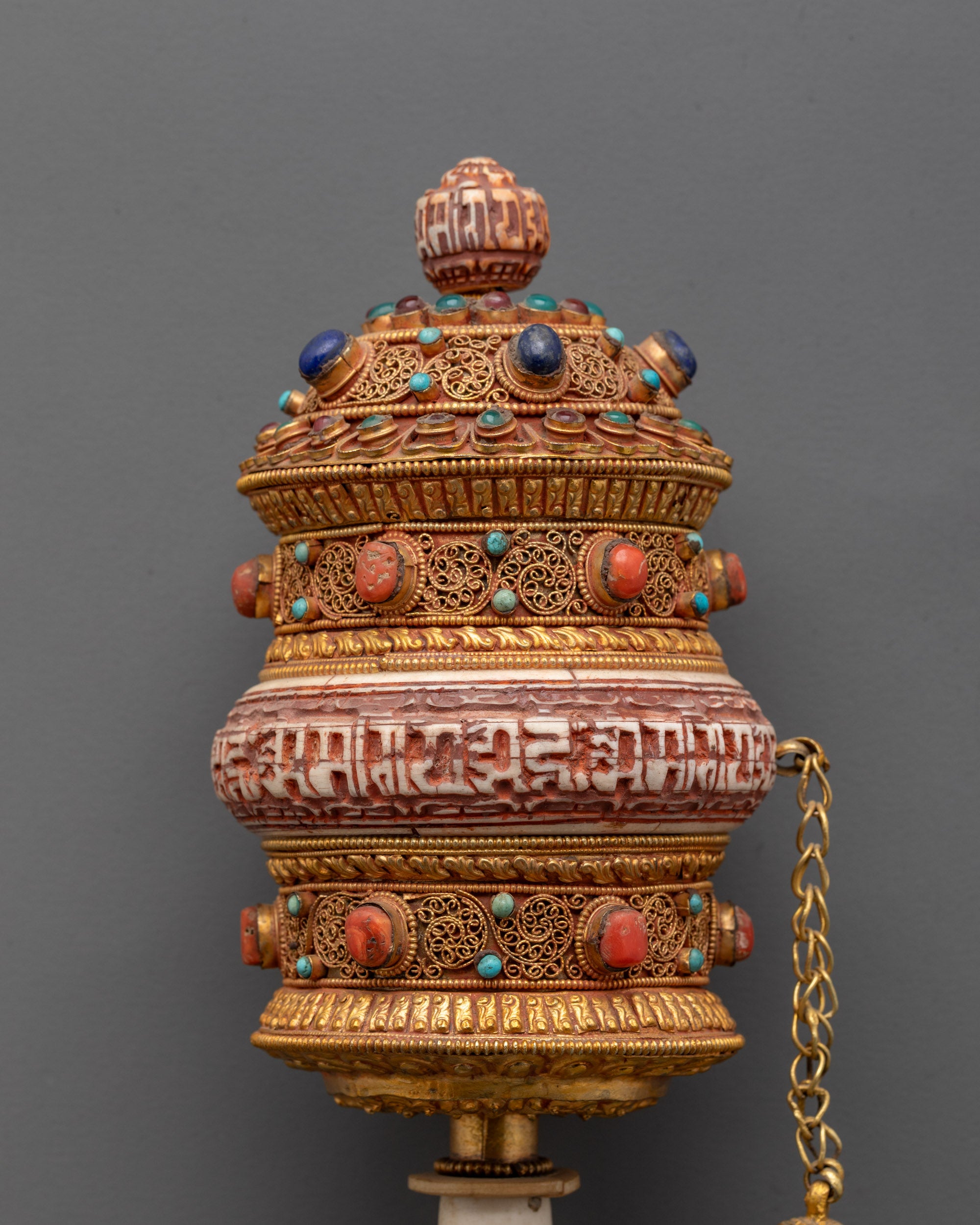 Close-up of handheld prayer wheel showing Om Mani Padme Hum engraving and vibrant stones