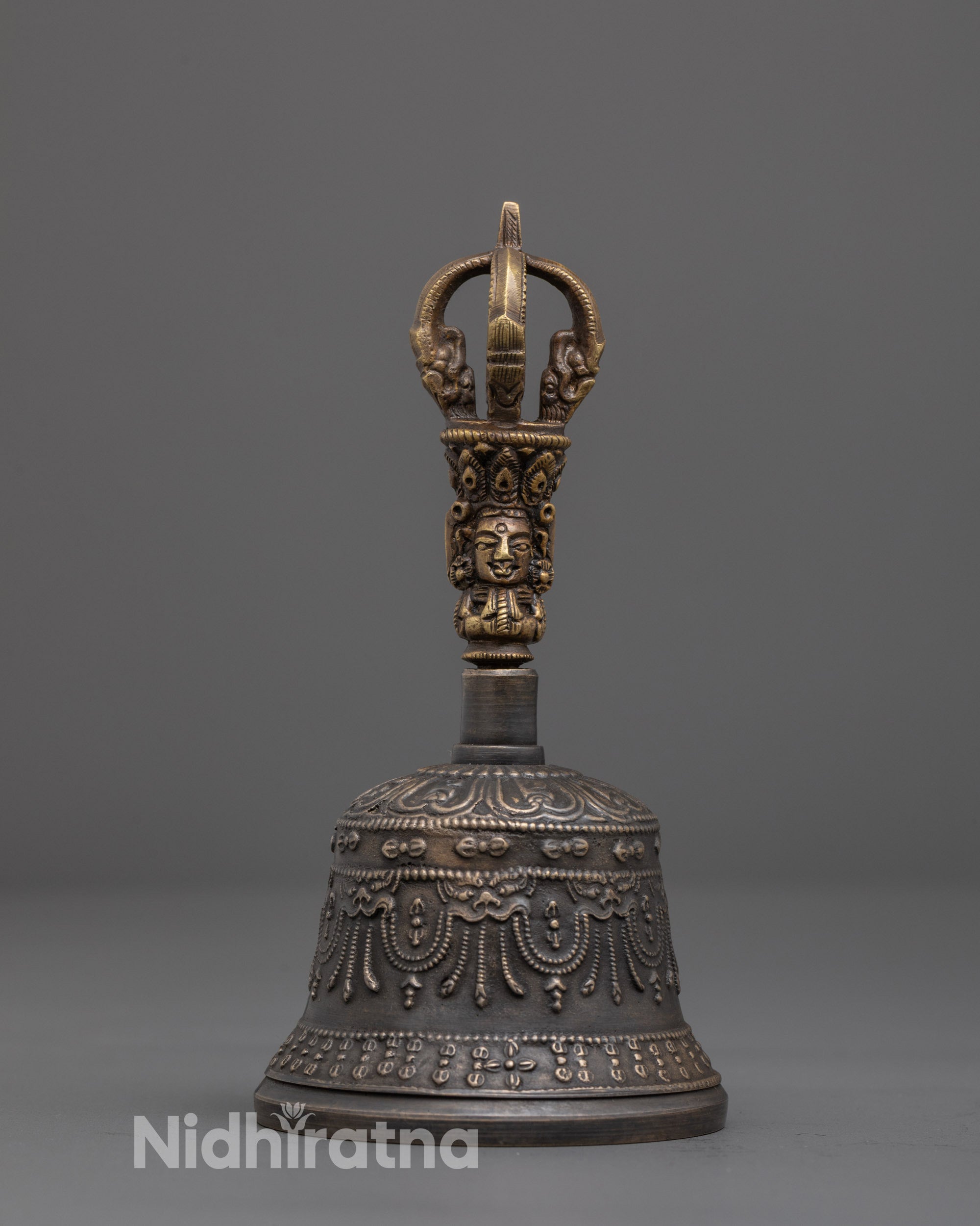 Close-up of intricate deity carving on brass handle of meditation bell
