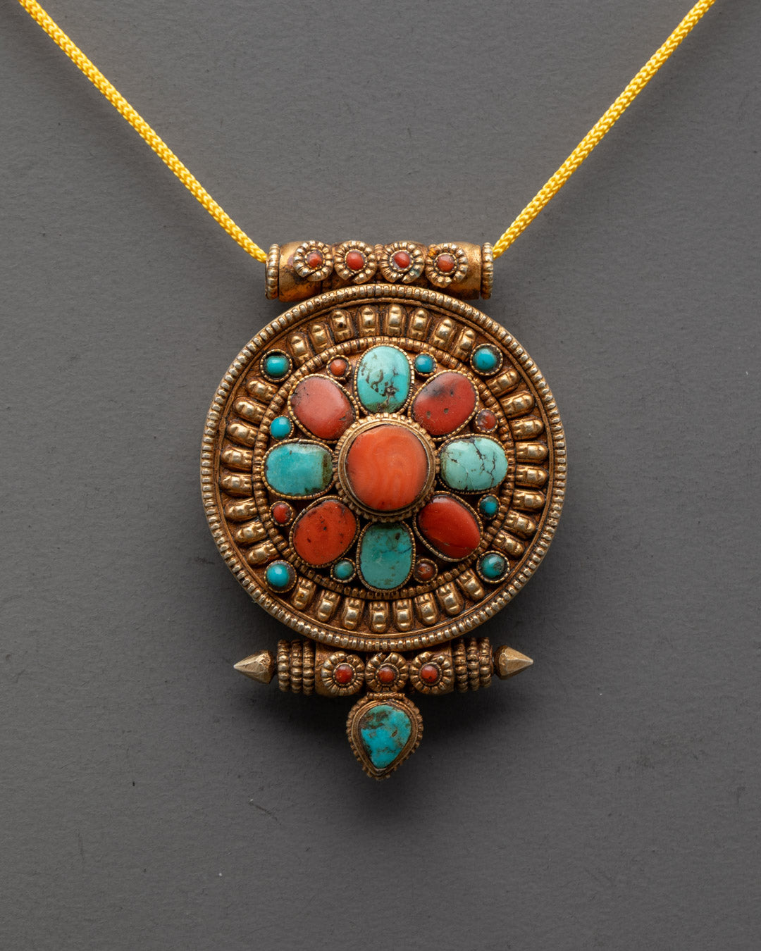 Close-up of intricately carved Himalayan amulet pendant showing detailed gold-gilded design

