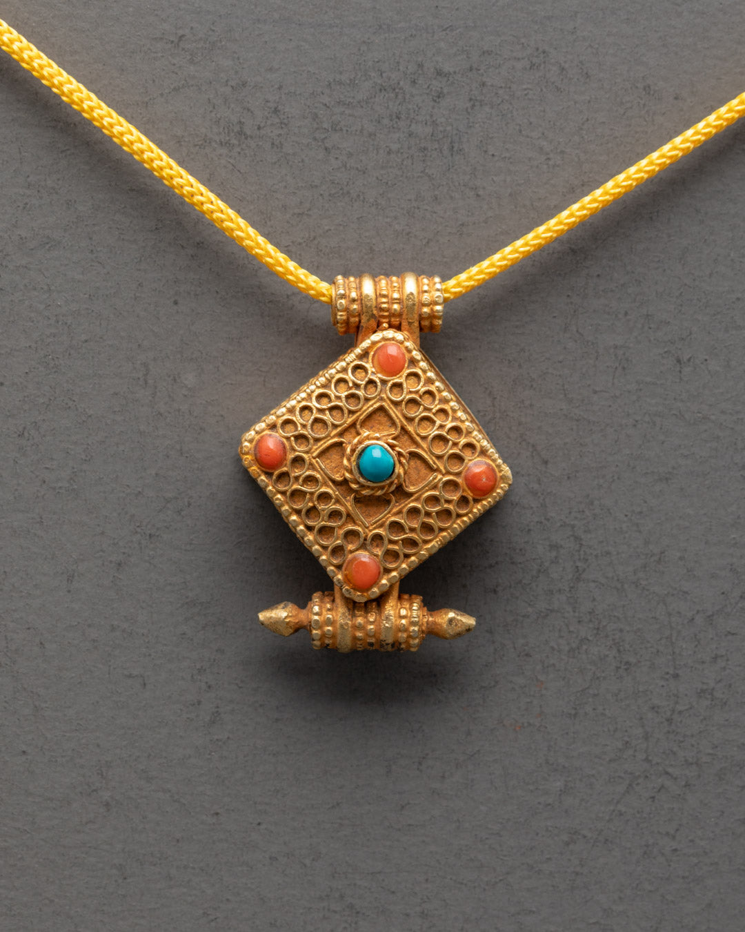 Close-up of intricately carved Tibetan amulet pendant showcasing detailed gold-gilded patterns

