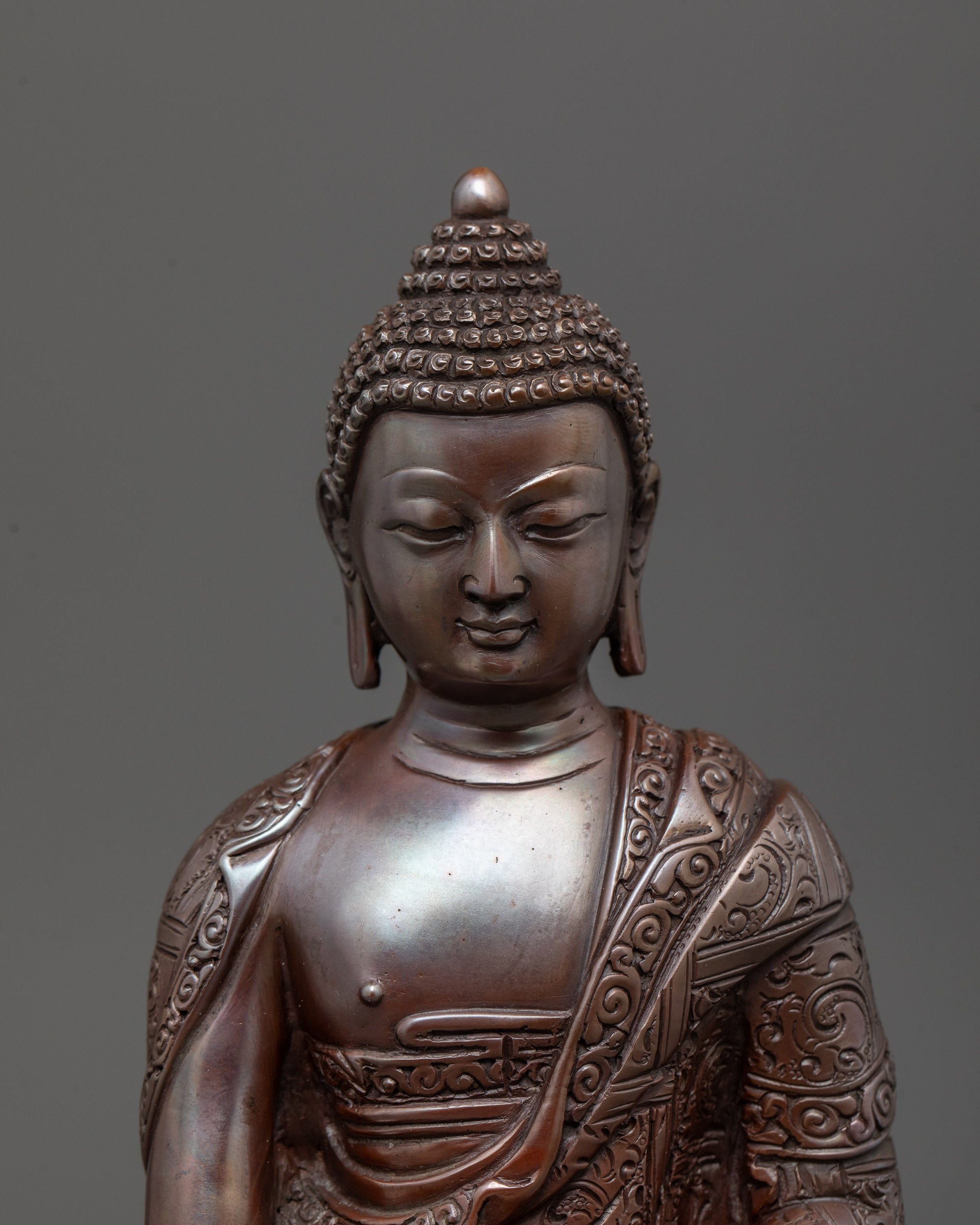 Close-up of oxidized copper Buddha statue showing intricate carved patterns and monk’s robe