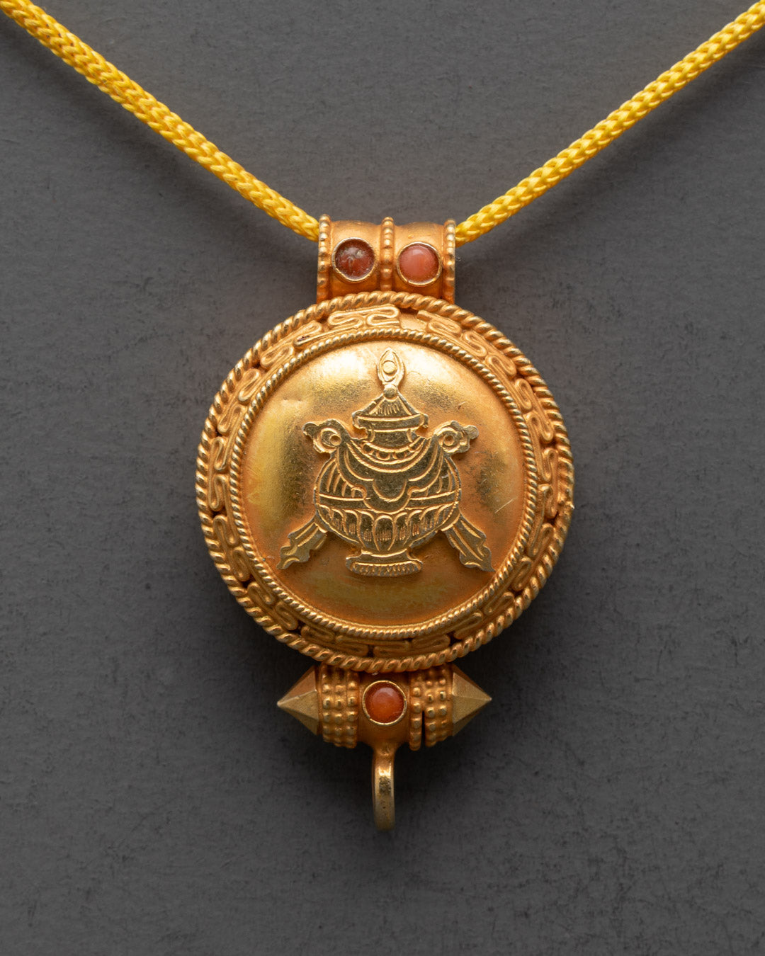 Close-up of sacred Bumpa design carved on gold-gilded Tibetan pendant locket

