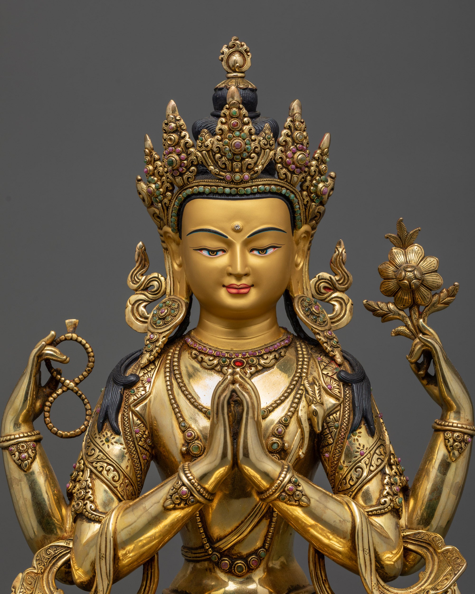 Close up Chenrezig statue with four arms holding lotus, crystal rosary, and wish-fulfilling jewel
