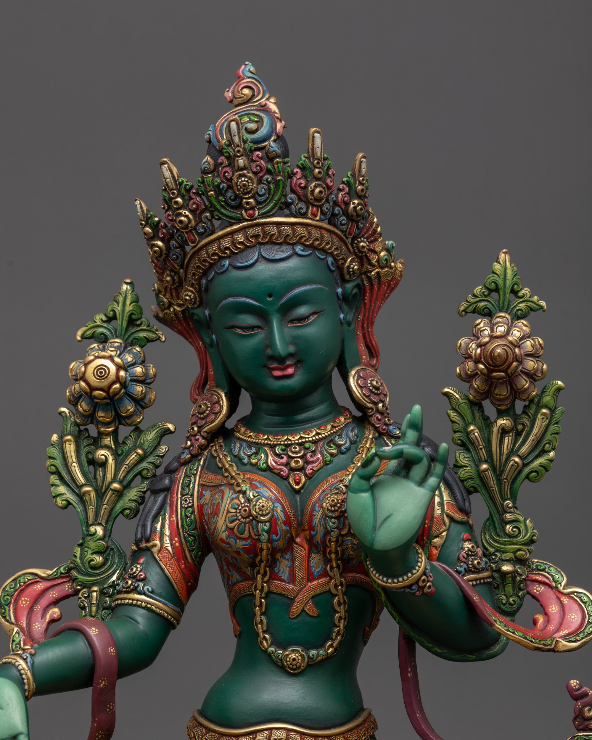 Close up Green Tara statue holding utpala flower with intricately painted lower garment

