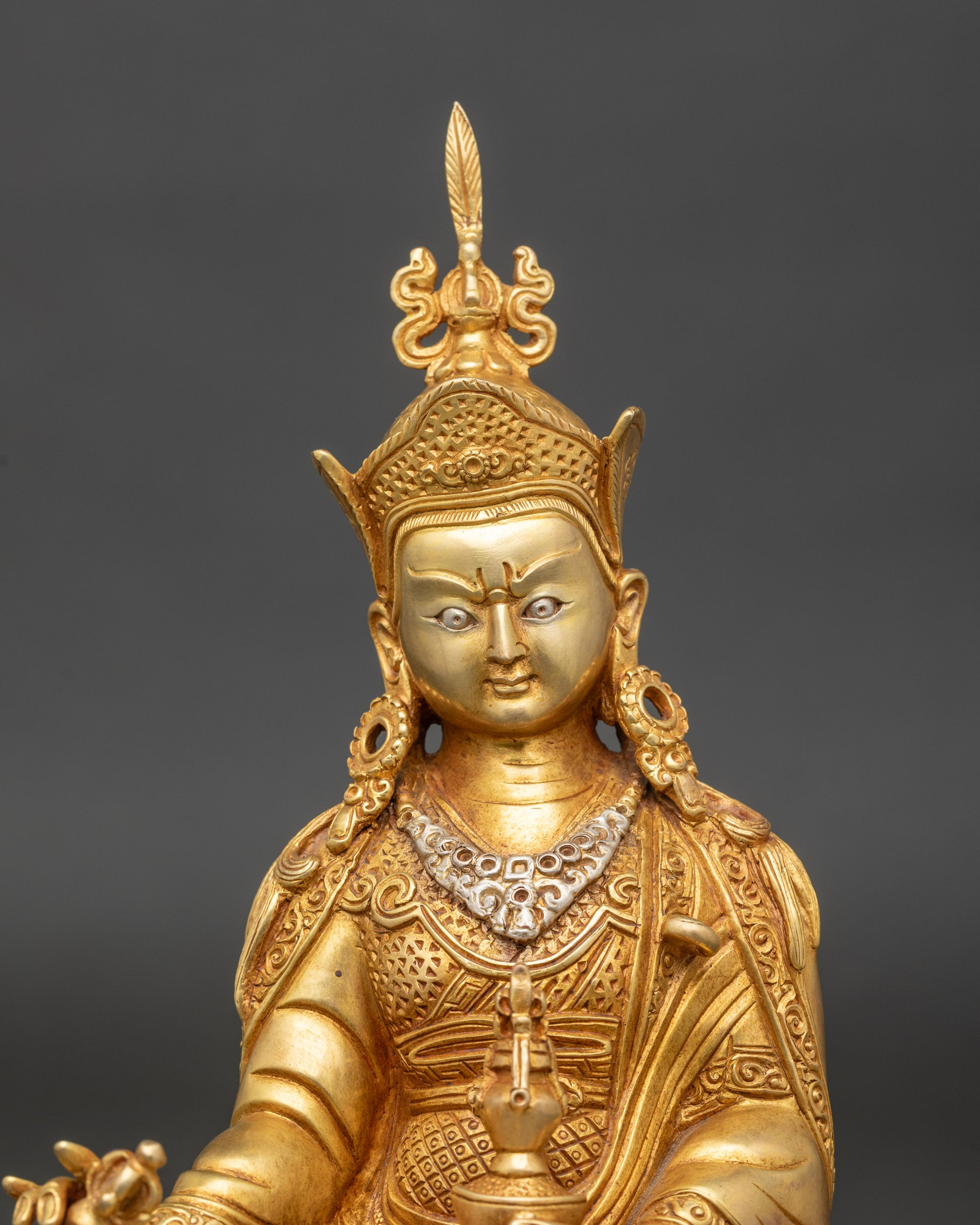 Close up Guru Rinpoche face with gold-painted details and intricate ceremonial robes