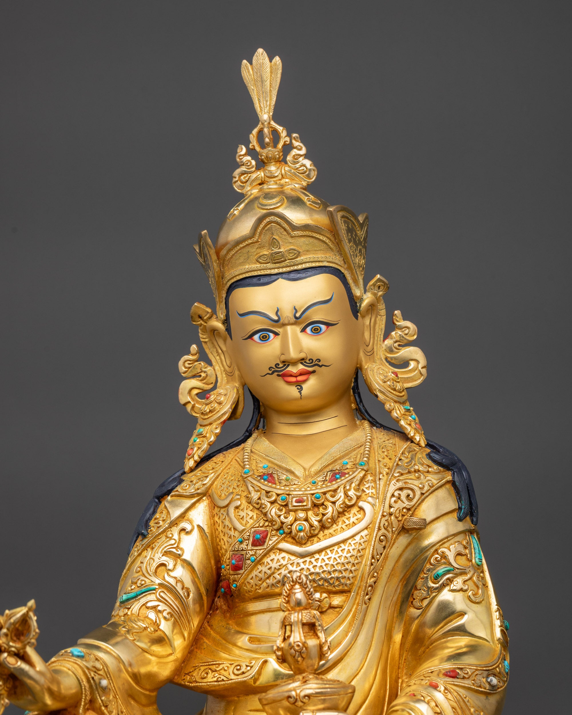 Close up Guru Rinpoche statue gold-gilded face wearing lotus crown with detailed carving