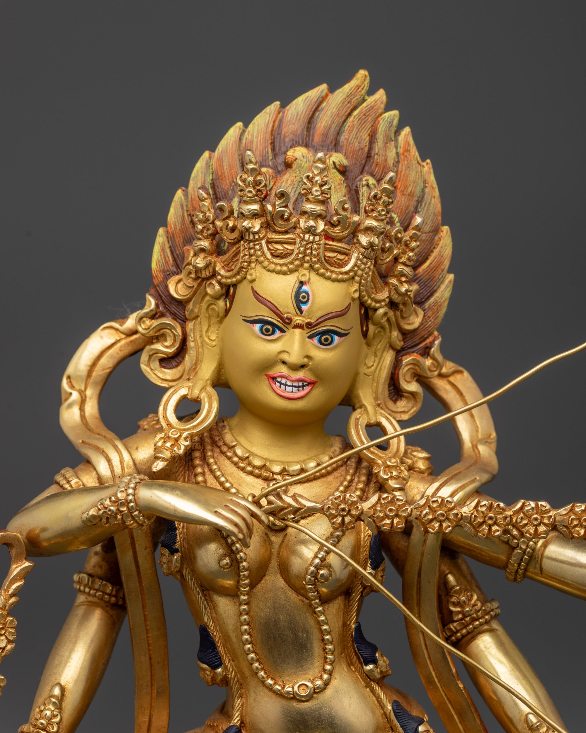 Close up Kurukulla statue showing third eye, five-skull crown, and sacred objects in hands
