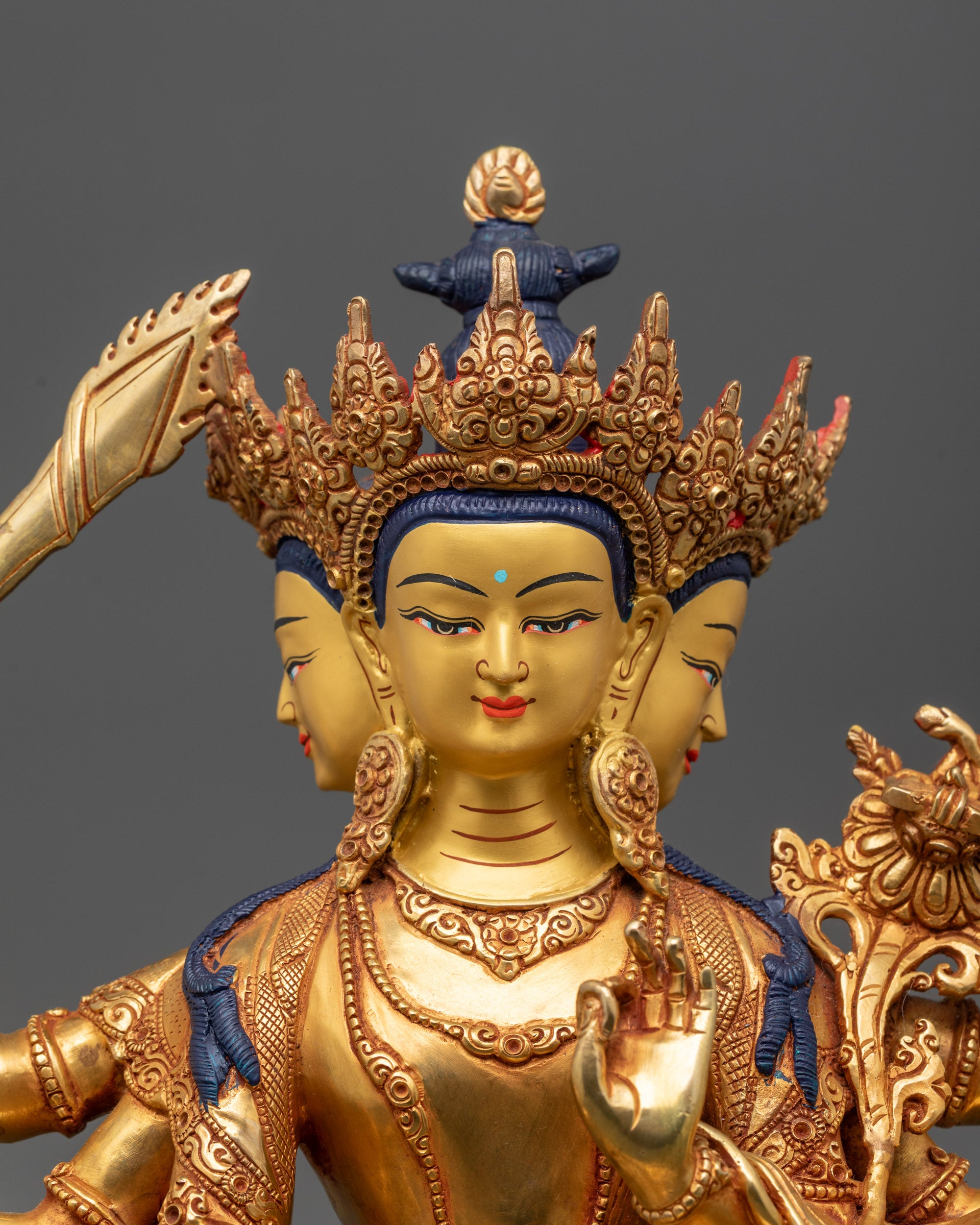 Close up Maha Manjushri Statue showing three gold-gilded faces and detailed carvings
