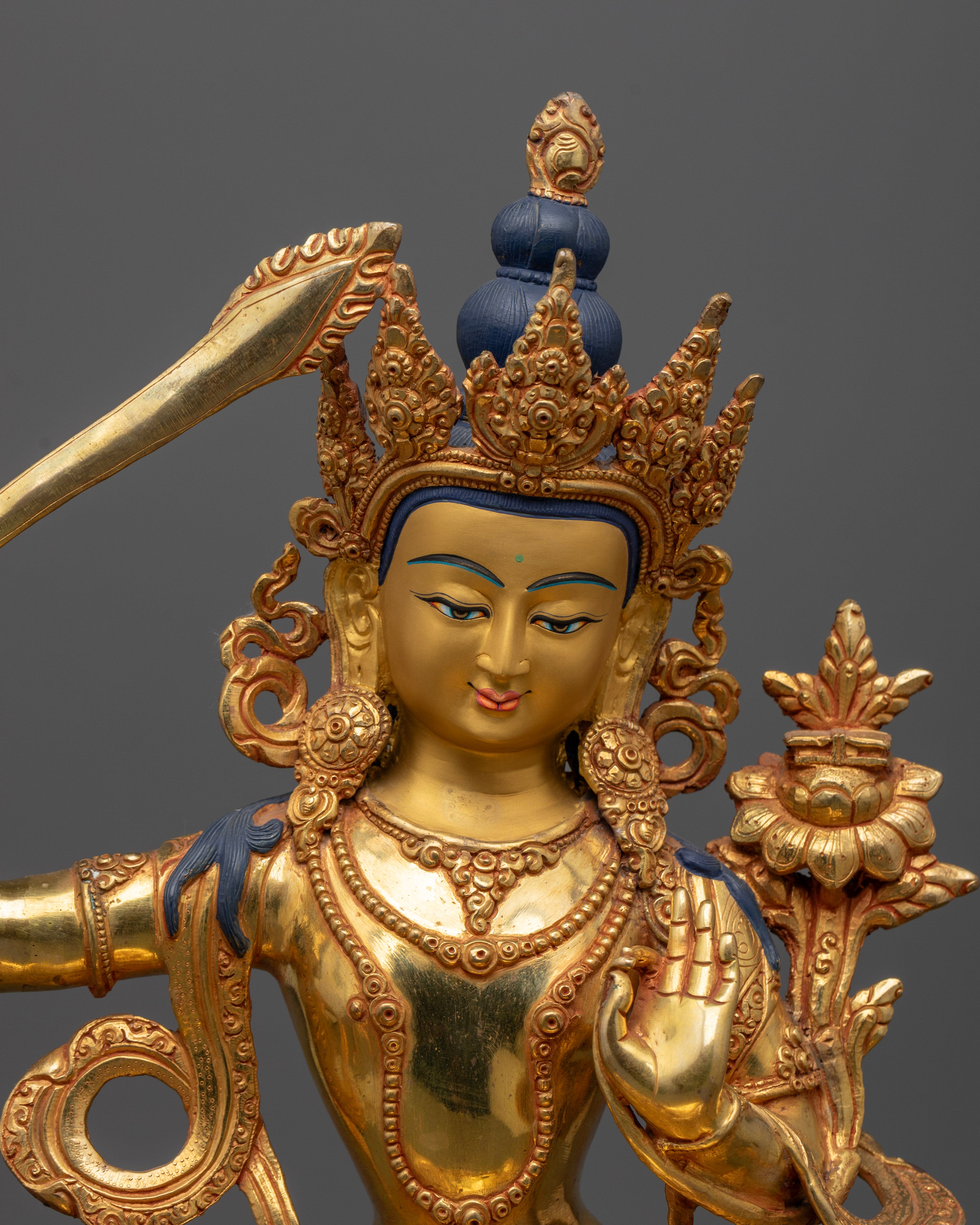 Close up Manjushri gold-painted face with wisdom sword and Utpala flower, hand-carved Newari Himalayan statue