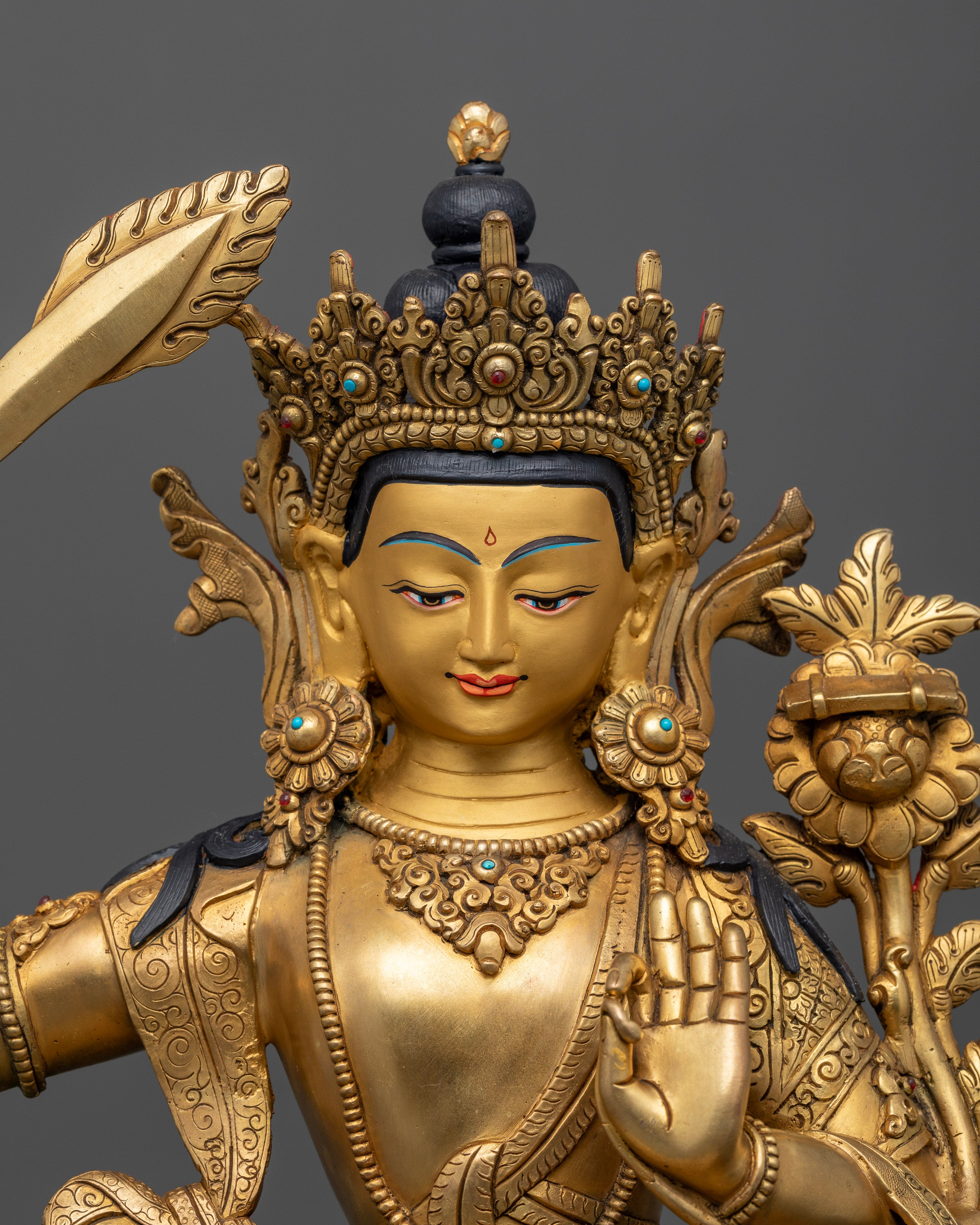 Close up Manjushri gold-painted face with wisdom sword and Utpala flower supporting Prajnaparamita Sutra, Himalayan sculpture