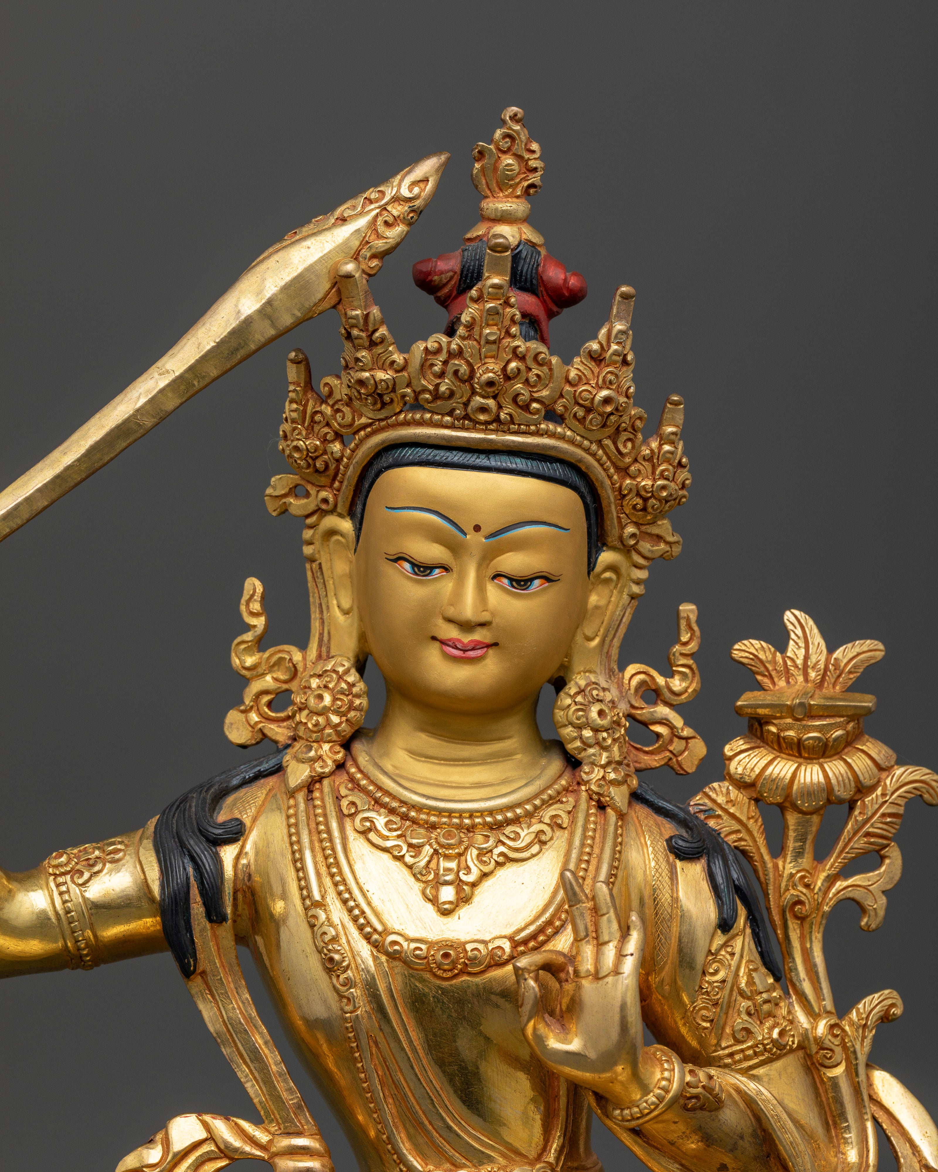 Close up Manjushri statue gold painted face wisdom sword utpala lotus Himalayan craft