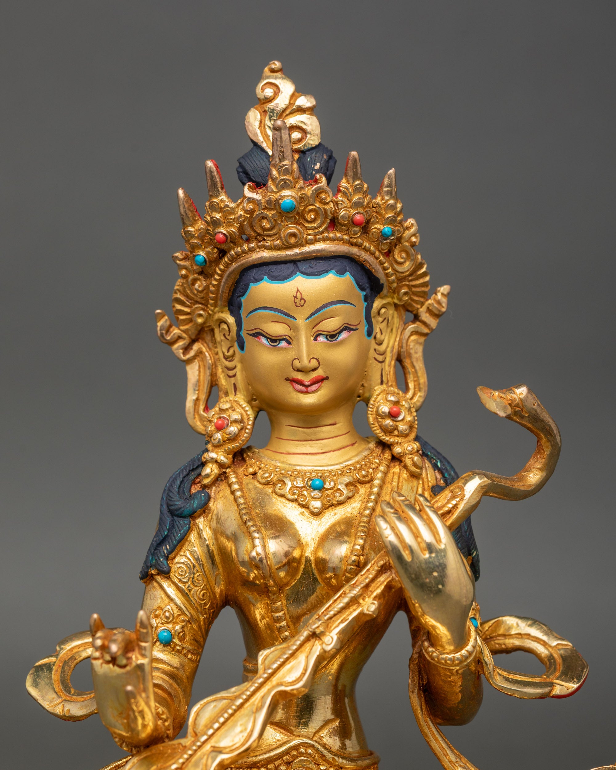 Close up Saraswati statue showing gold-painted face, detailed veena, and jeweled crown