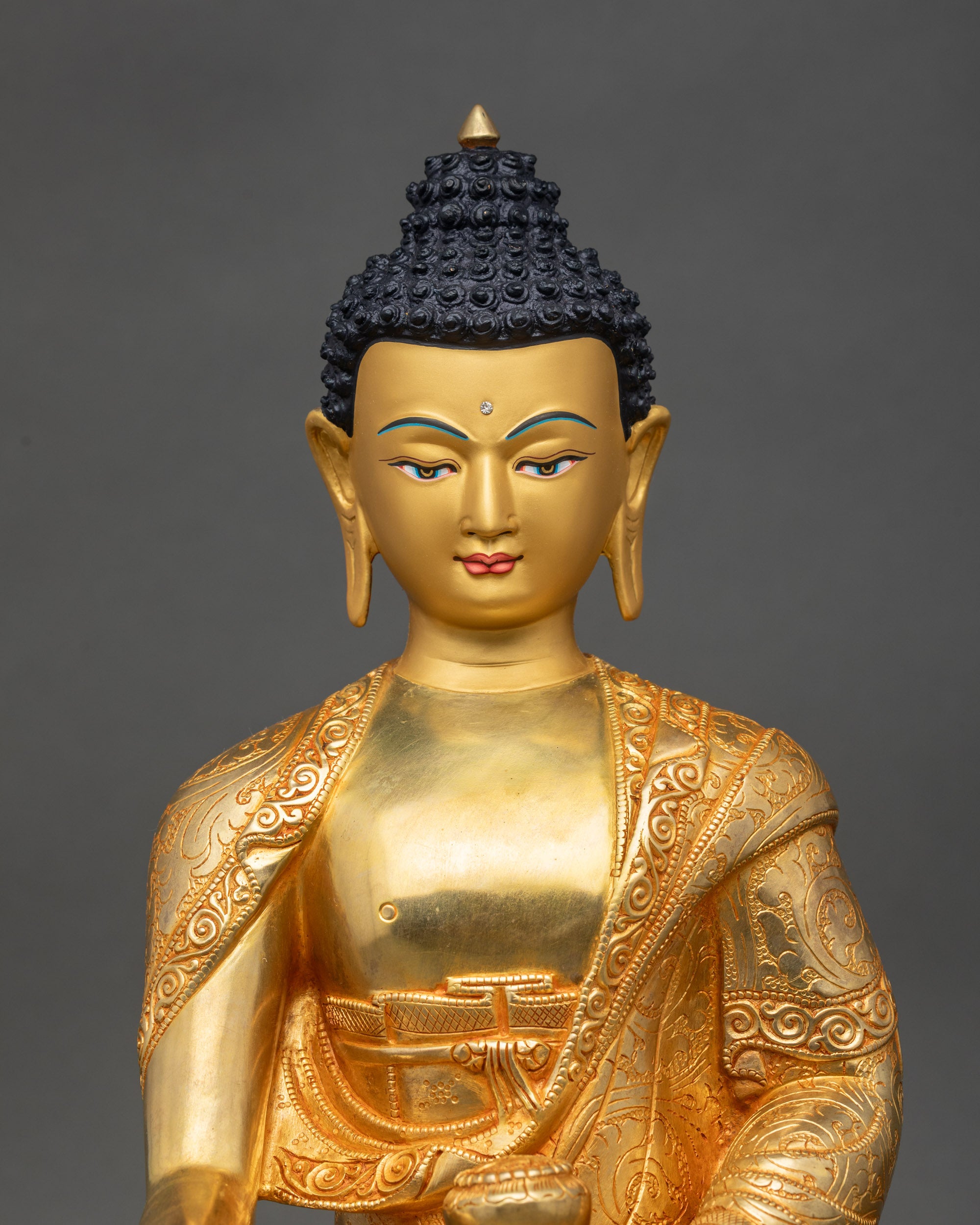 Close up Shakyamuni Buddha statue showing gold-painted face, intricate robes, and details