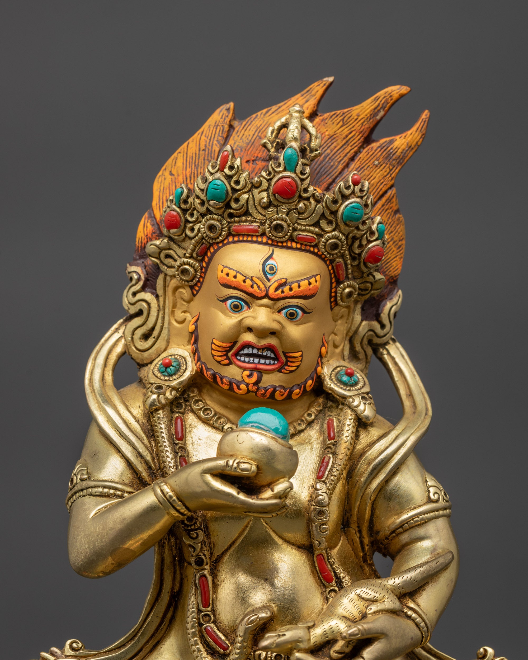 Close up gold-gilded face of Black Dzambhala with third eye and jeweled spitting mongoose