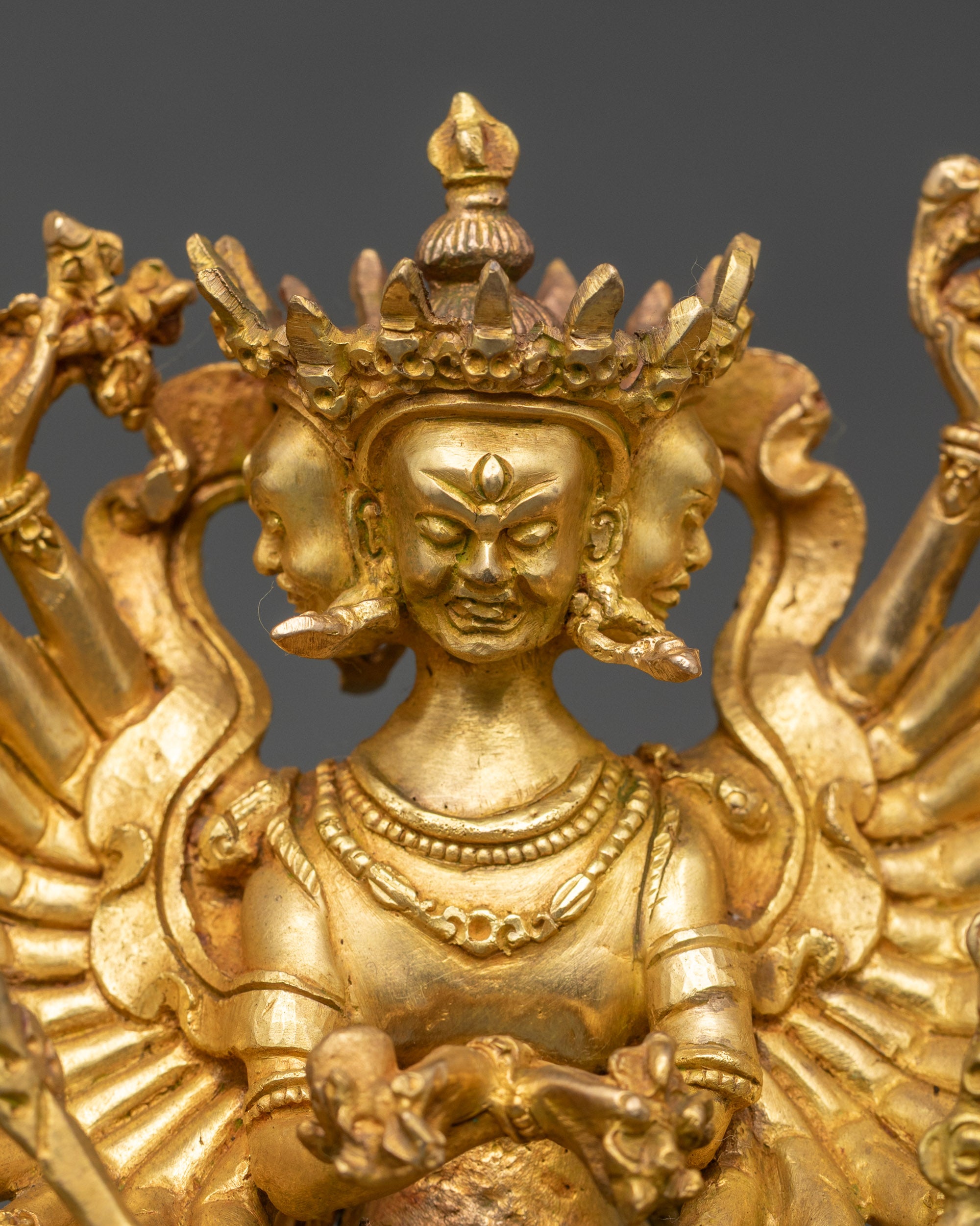 Close up gold-painted faces twenty-four arms Himalayan tantric meditation sculpture