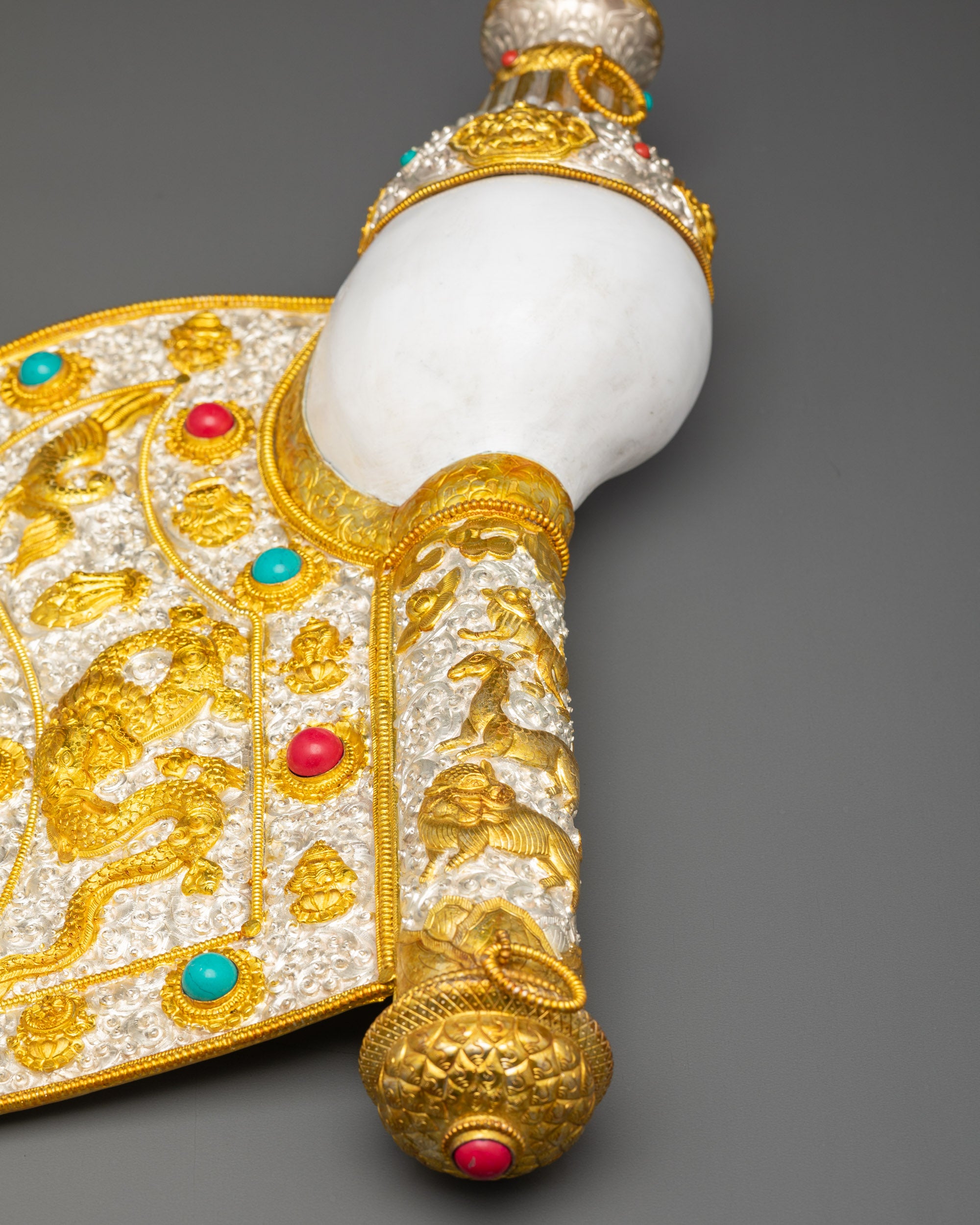 Close up gold and silver-plated conch shell showing coral, turquoise, and mythical creatures