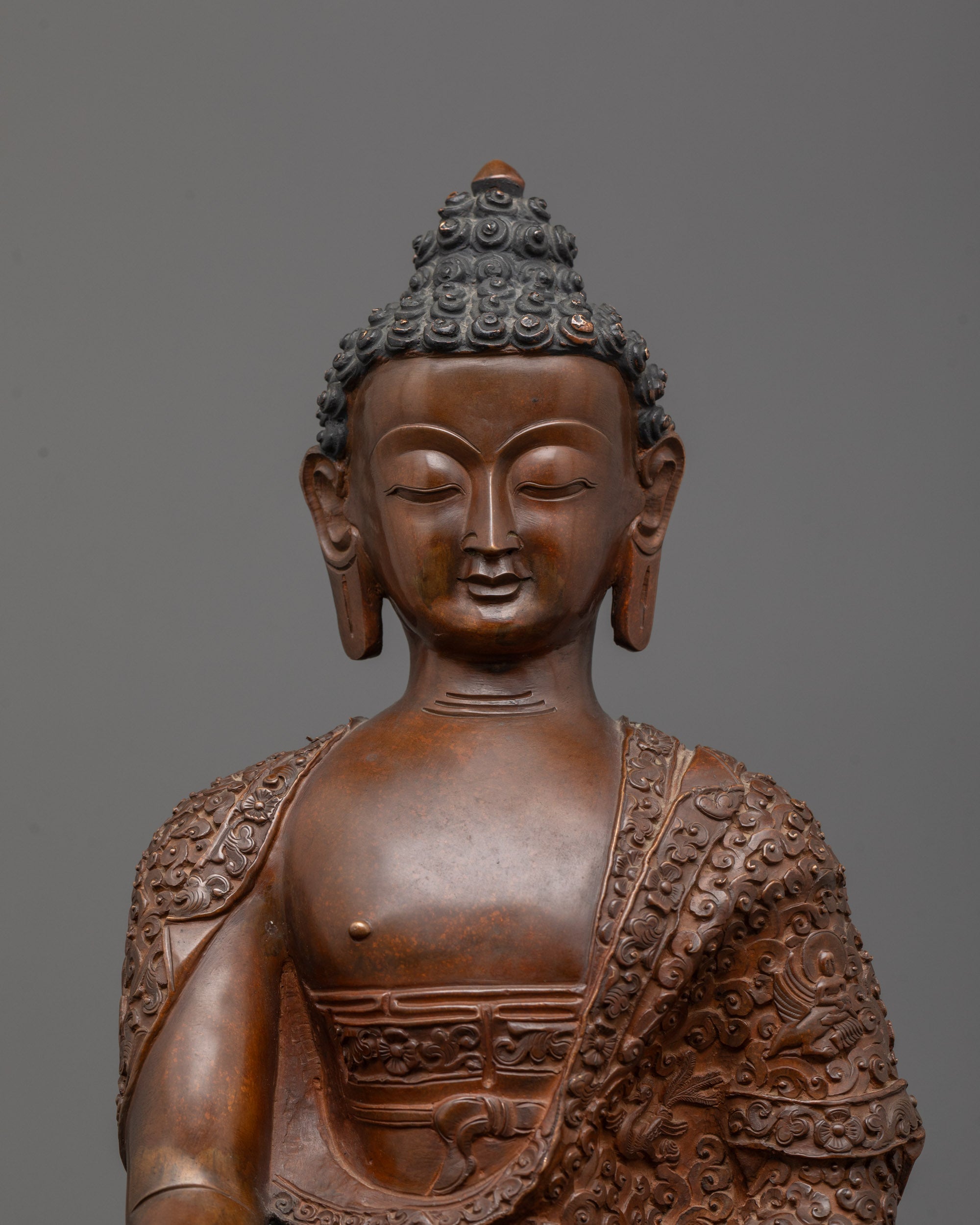 Close up of Buddha’s oxidized copper face and alms bowl in earth-touching mudra.