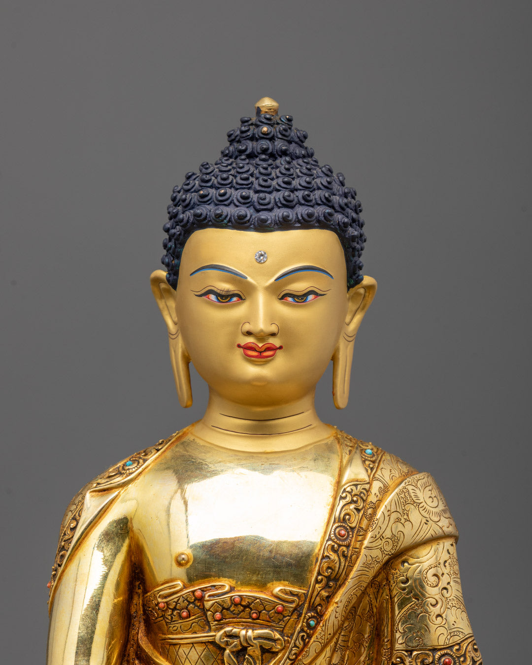 Close up of Buddha statue’s gold-gilded face and semi-precious stone decorations
