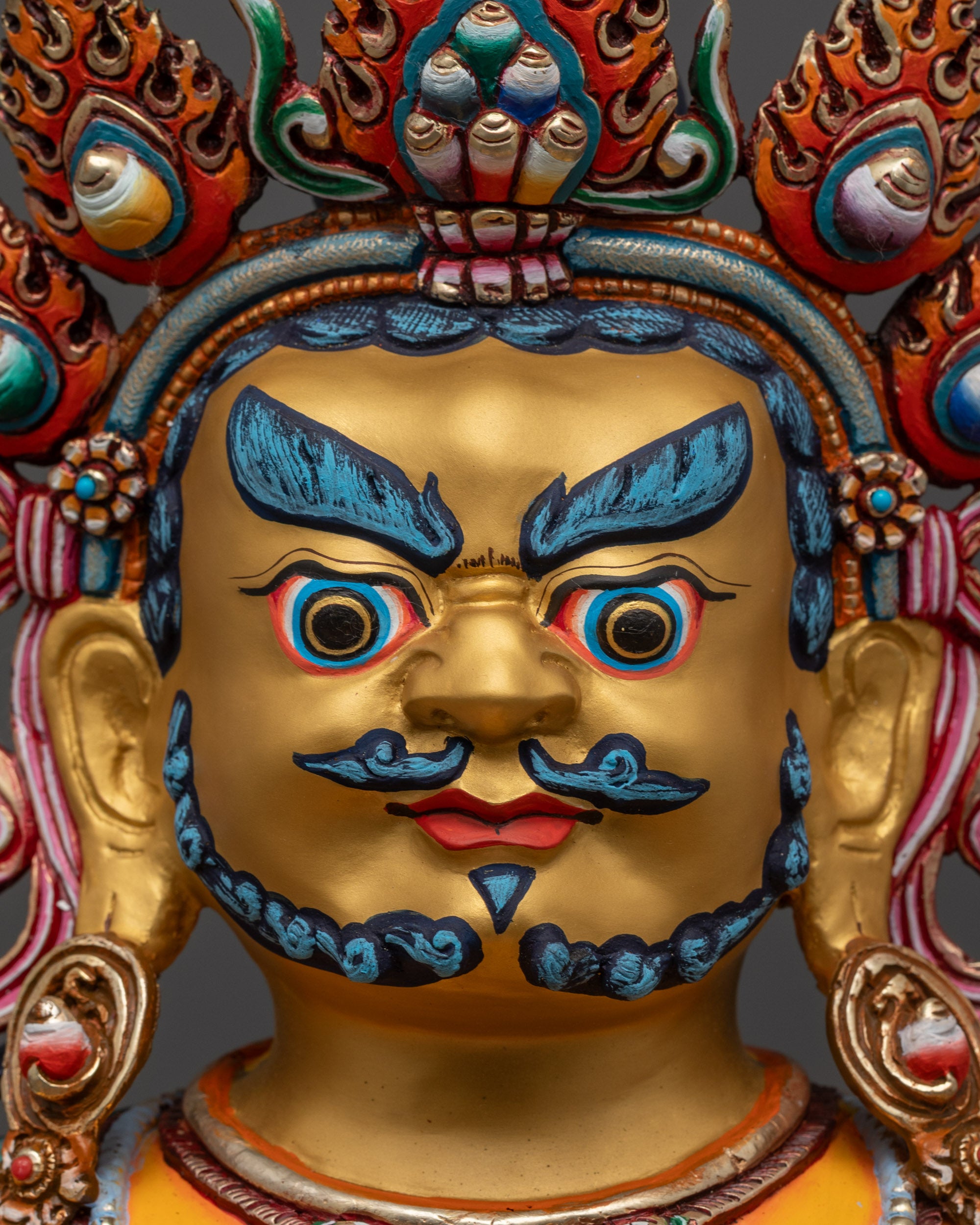 Close up of Dzambhala sculpture showing gold-gilded face, shell crown, and jeweled adornments