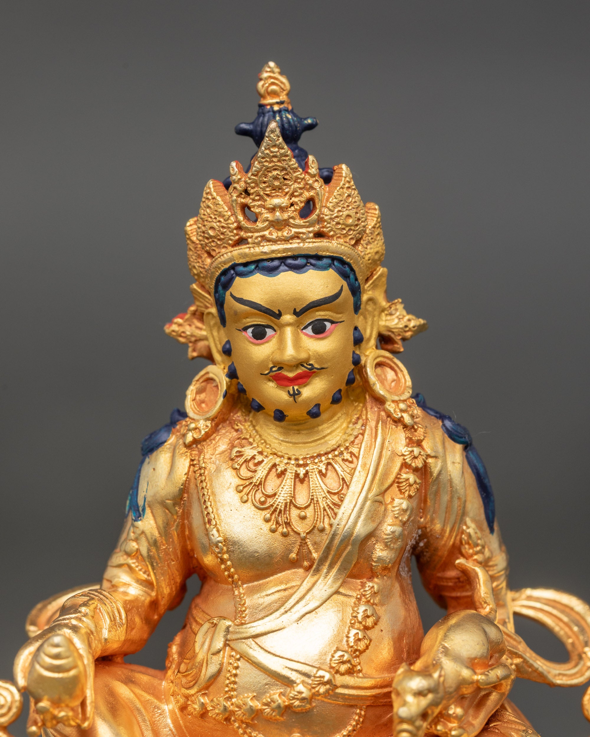 Close up of Dzambhala statue gold face and intricate fire-gilded details on garments