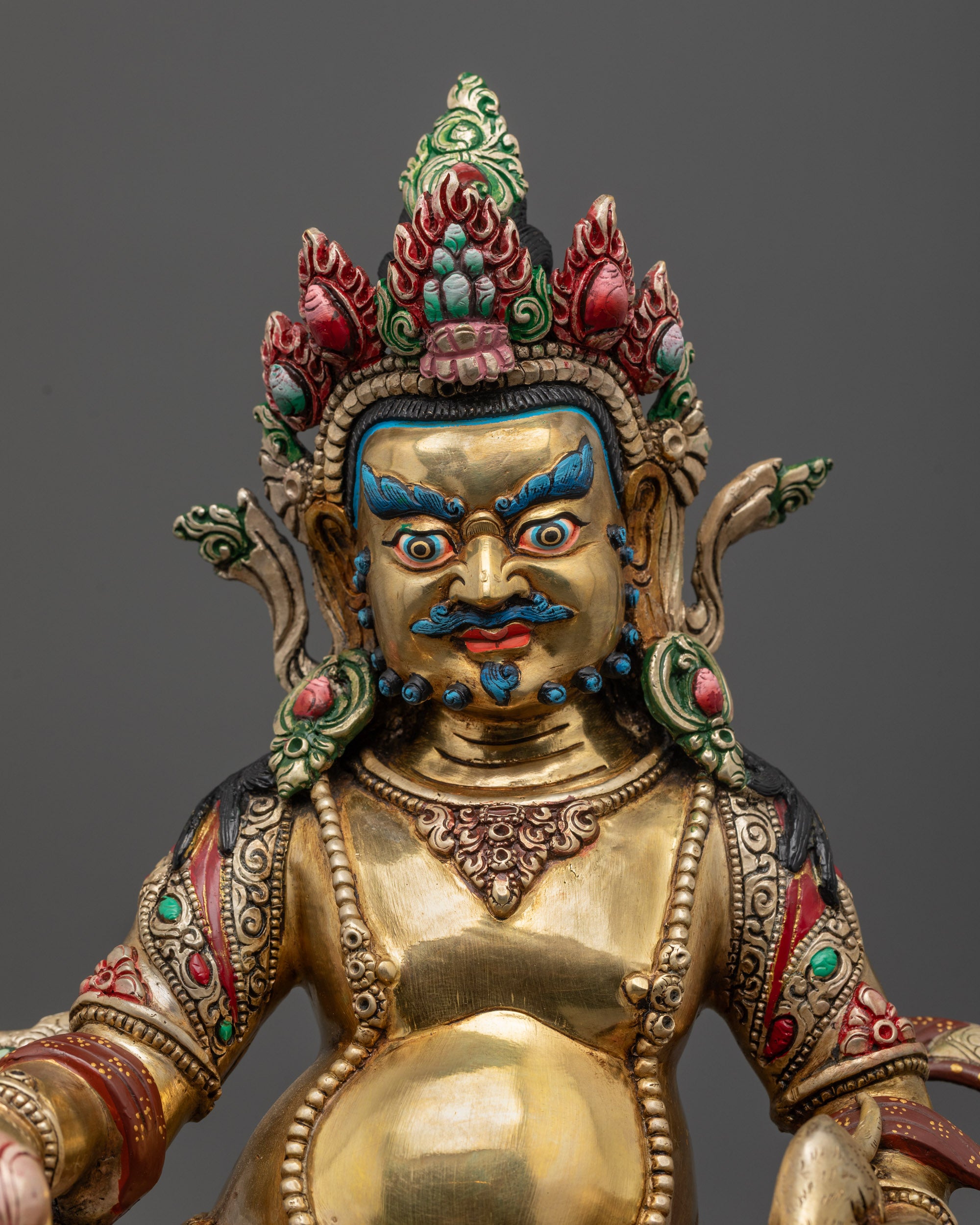 Close up of Dzambhala statue showing vibrant shell crown, jewelry, and semi-precious stones
