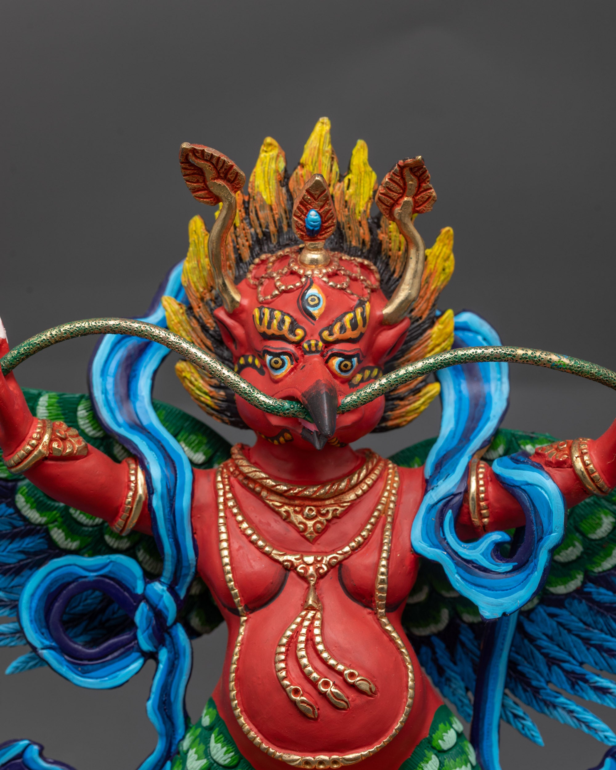 Close up of Garuda's wrathful face with five-skull crown and intricate jewelry

