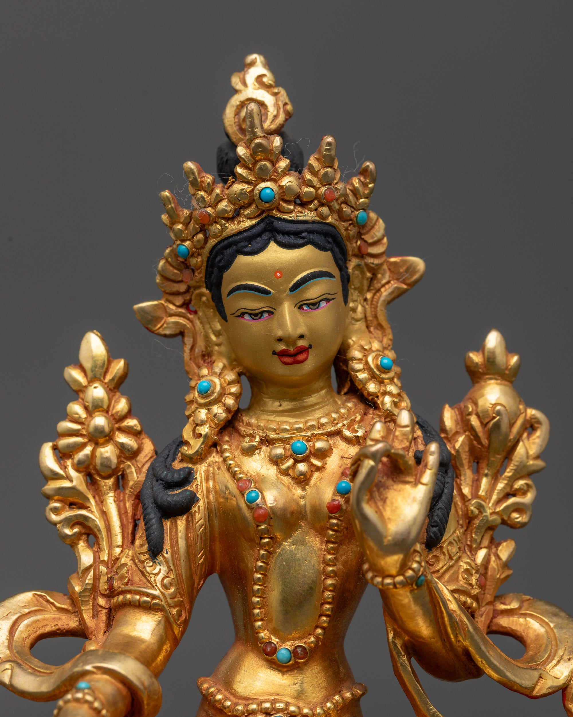 Close up of Green Tara statue showing serene face, crown, and detailed flowing robes
