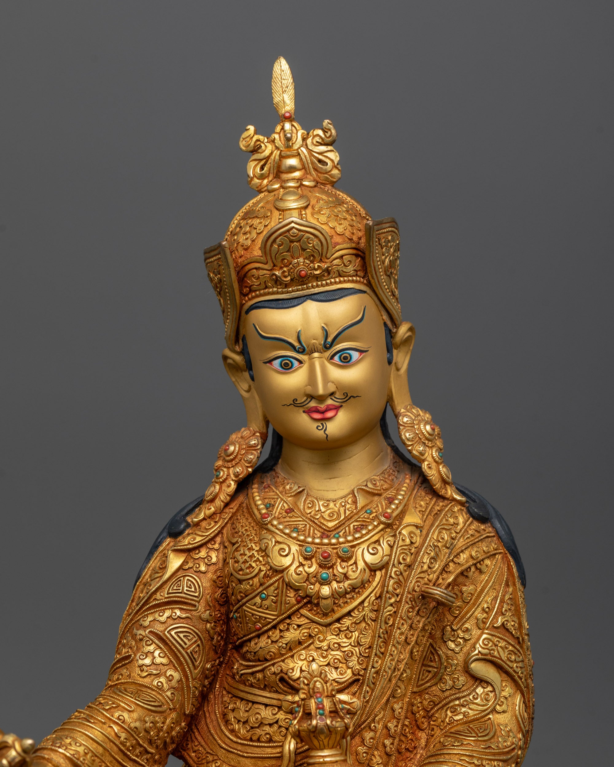 Close up of Guru Rinpoche statue showing gold-gilded face and intricate robe carvings