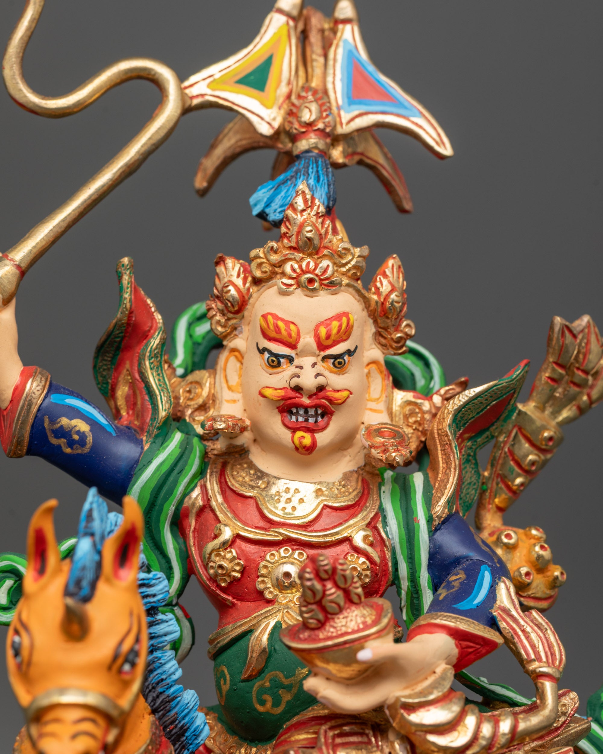 Close up of King Gesar statue showing kapala staff and detailed attire with intricate painting