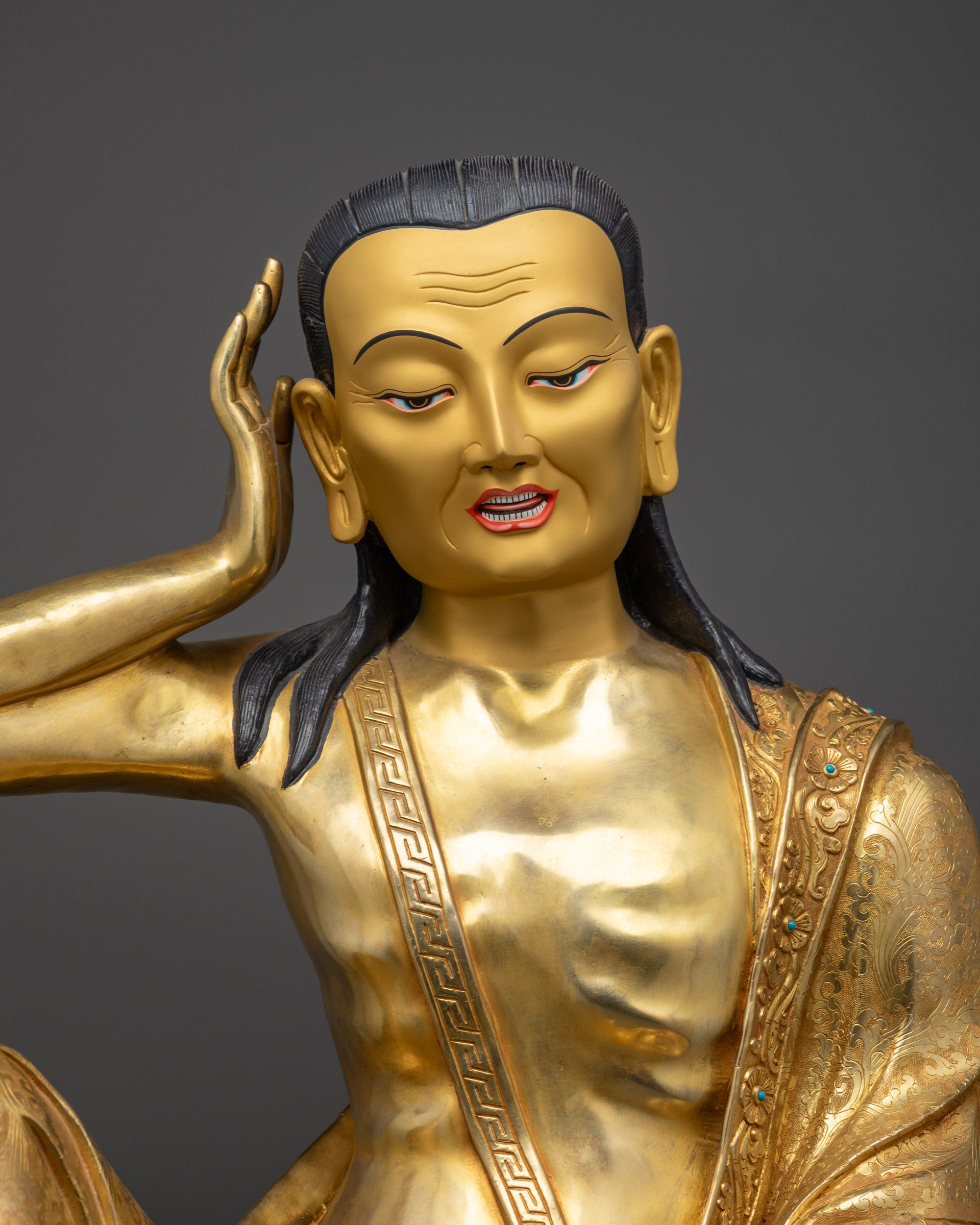 Close up of Milarepa statue showing carved robes, ornate patterns, and gemstone details
