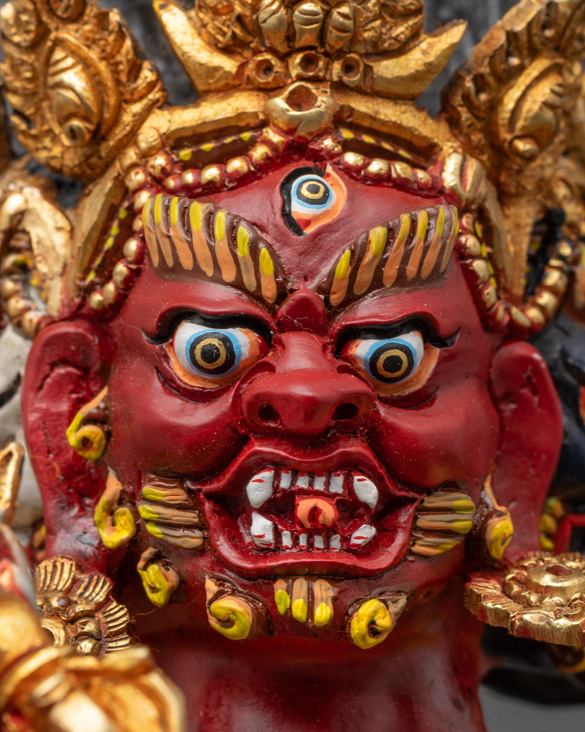 Close up of Red Dzambhala face showing wrathful expression and detailed gold jewelry
