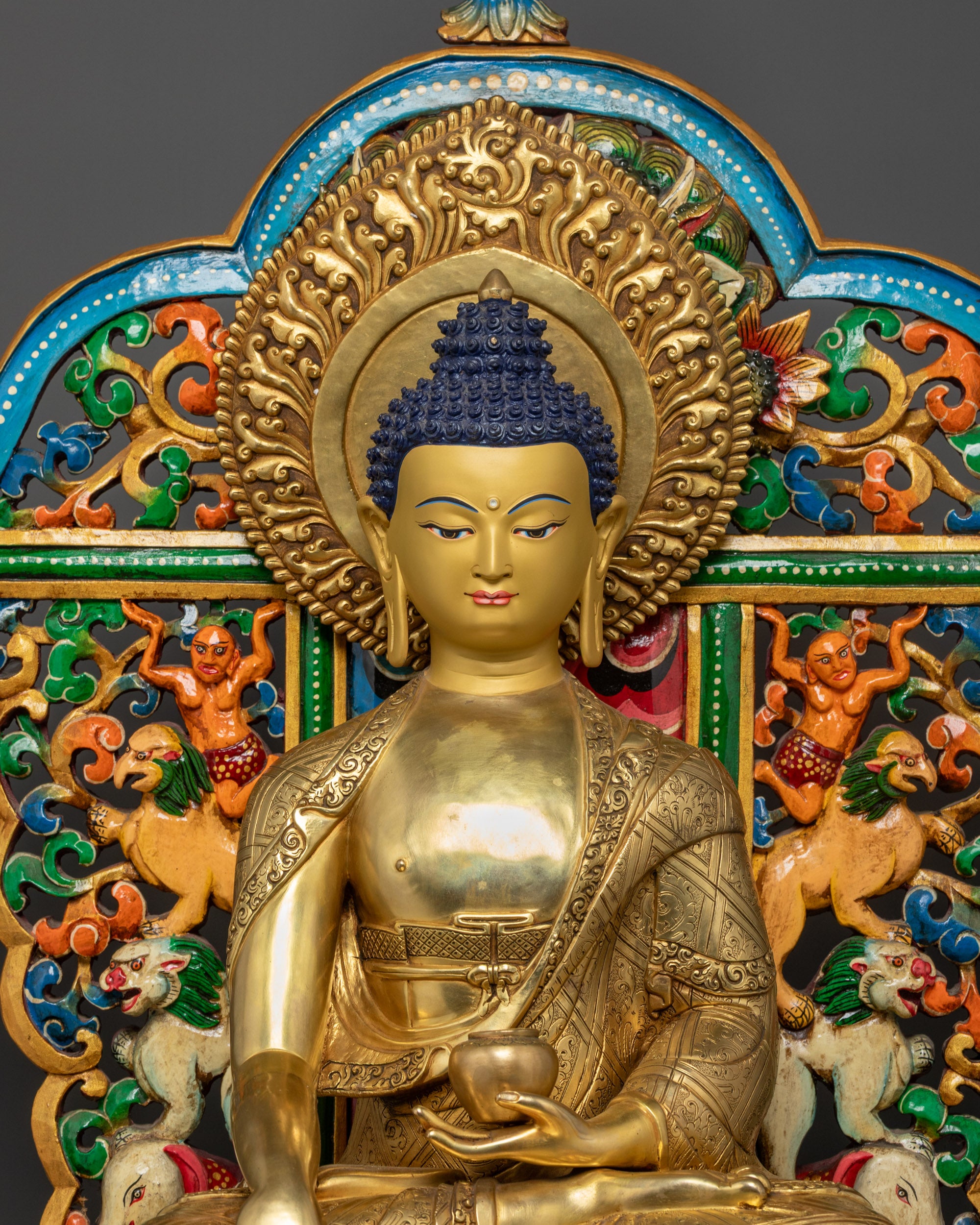Close up of Shakyamuni Buddha gold-gilded face and intricate monk robe patterns
