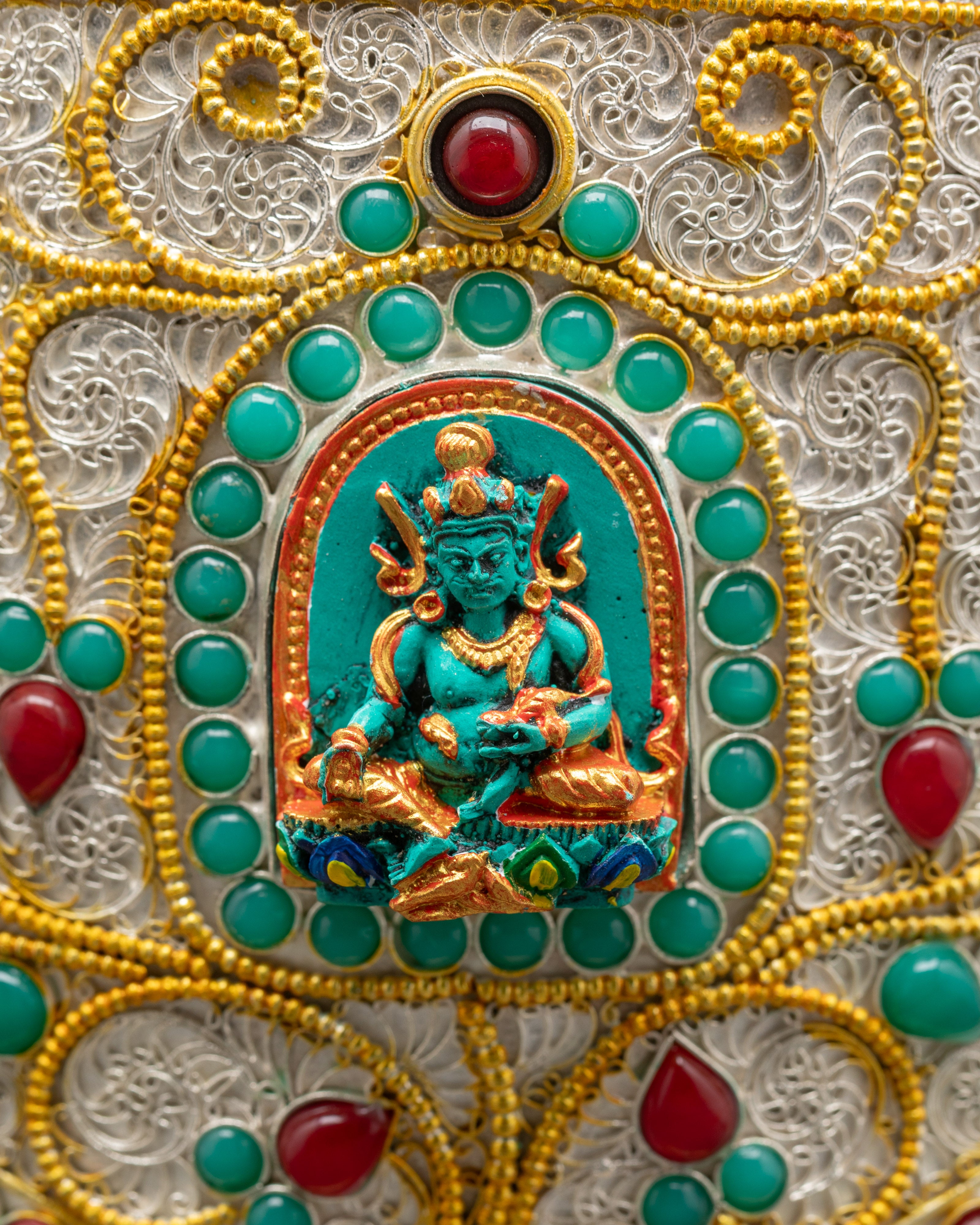 Close up of Tibetan rice pot showing Dzambhala carving with ruby turquoise emerald gems