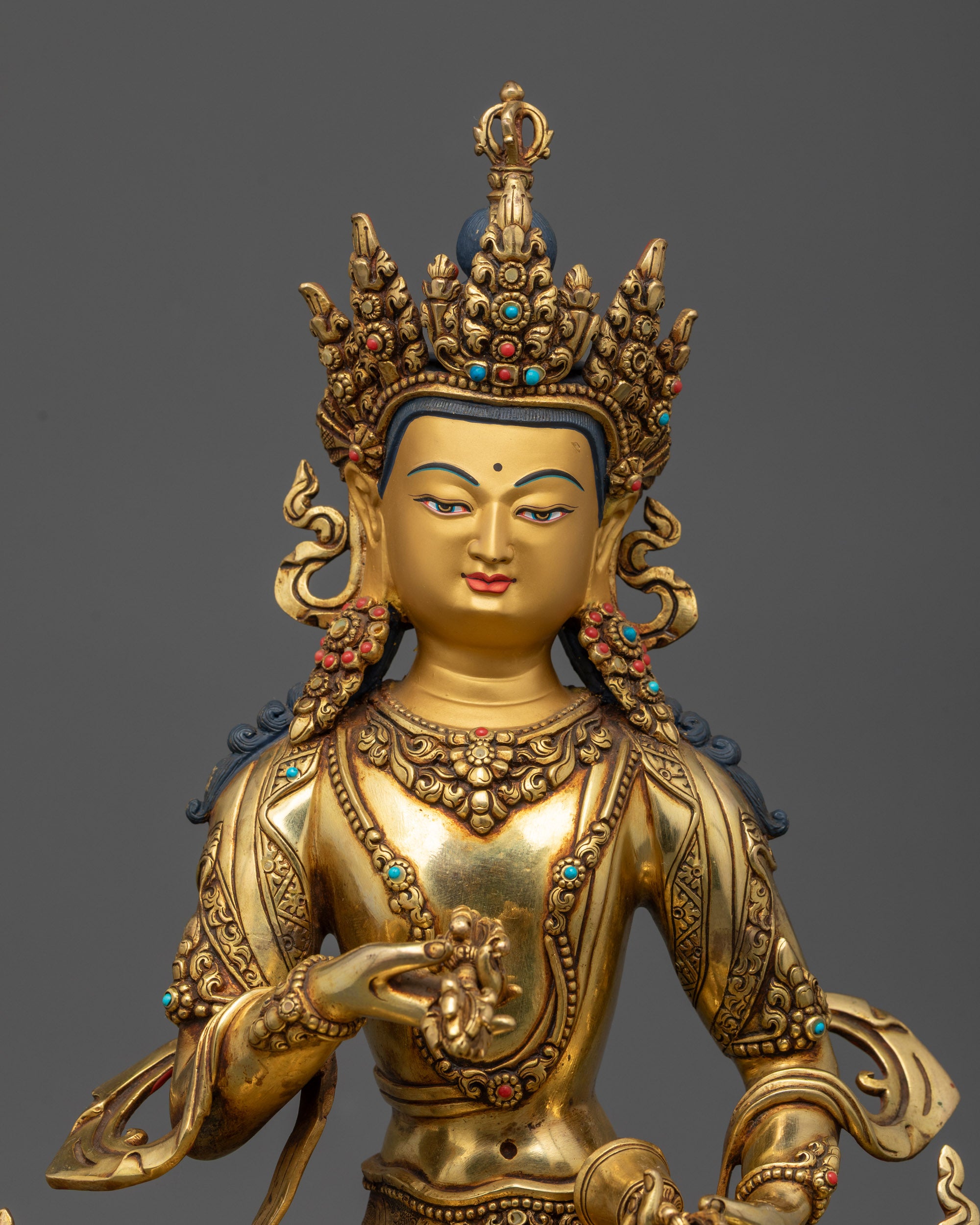 Close up of Vajrasattva Statue showing calm expression, Vajra, Ghanta, and stone-adorned robe