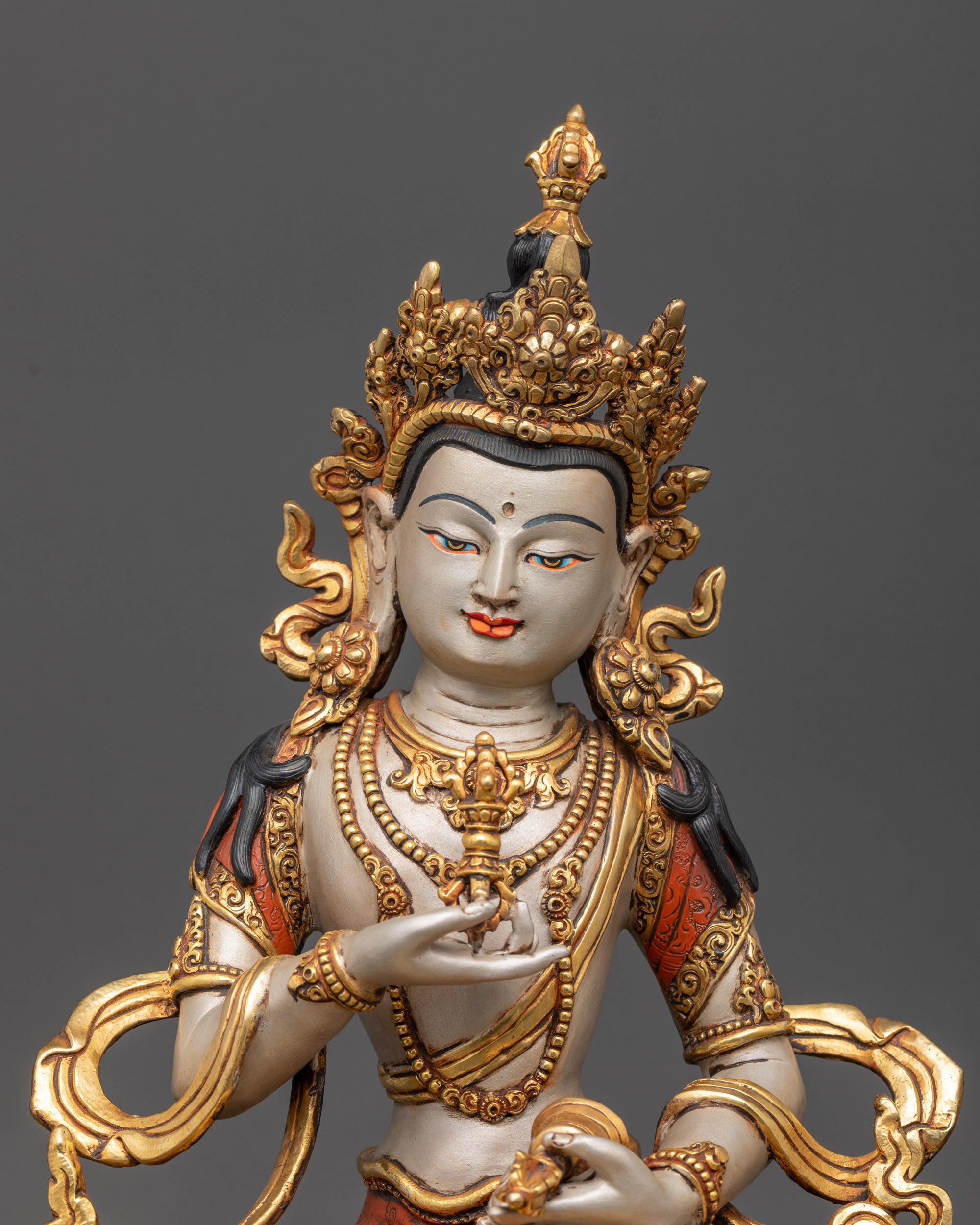Close up of Vajrasattva holding vajra and bell with intricate patterns on gold-plated robe