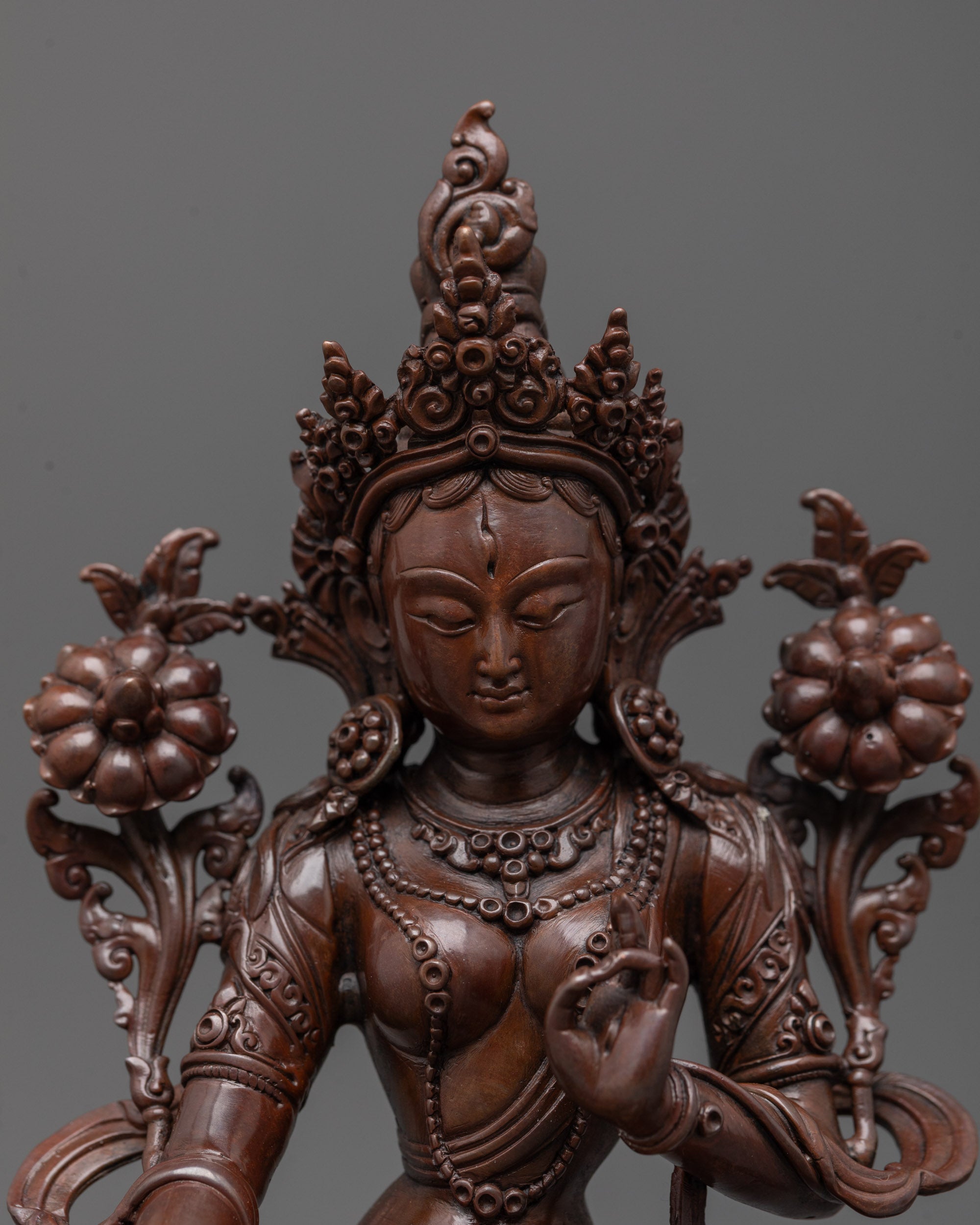 Close up of White Tara statue’s oxidized copper face holding utpala flowers in hand
