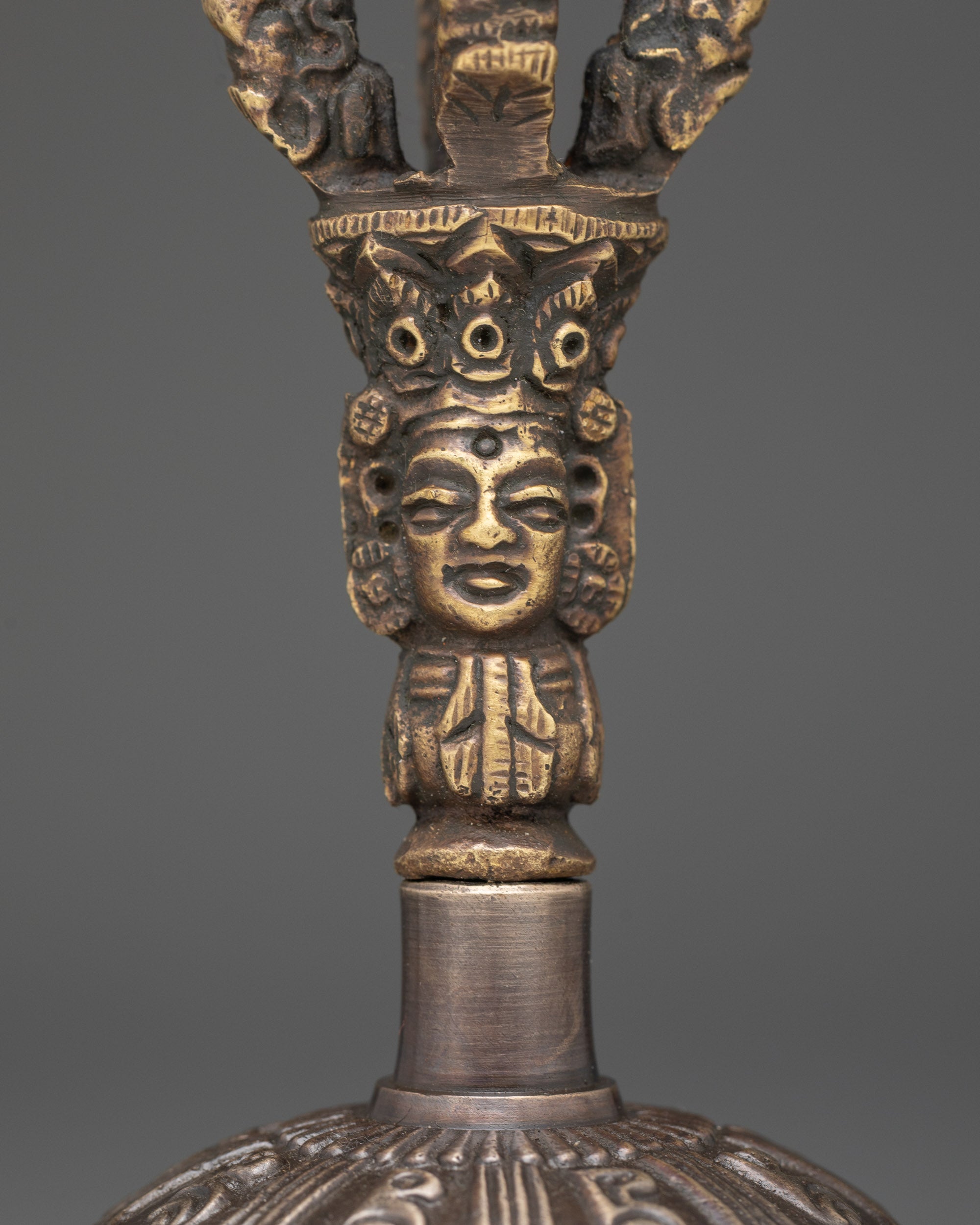 Close up of bell with deity handle and intricate bronze patterns for sacred rituals