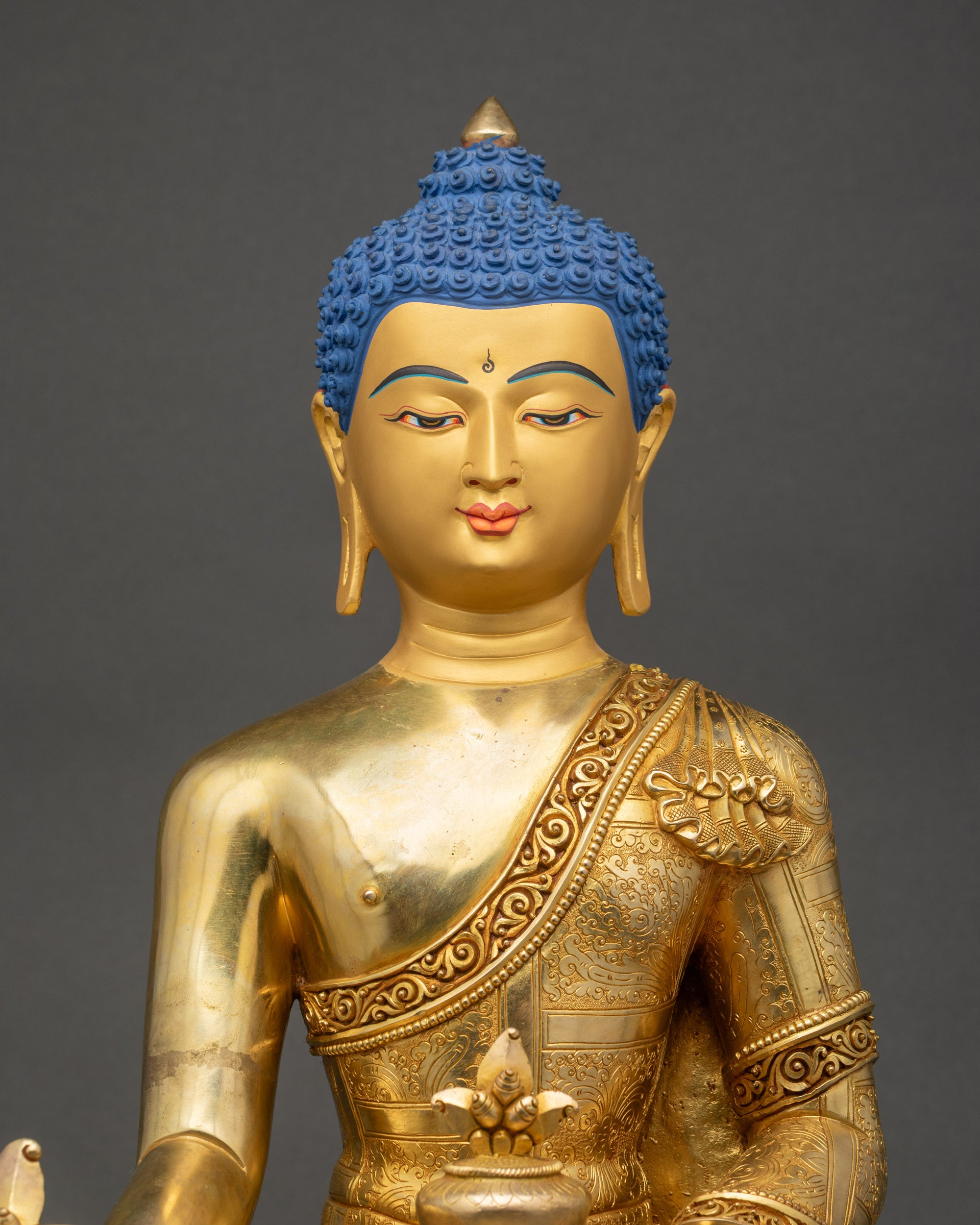 Close up of gold-gilded Medicine Buddha statue showing robe and halo details