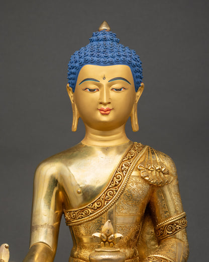 Close up of gold-gilded Medicine Buddha statue showing robe and halo details