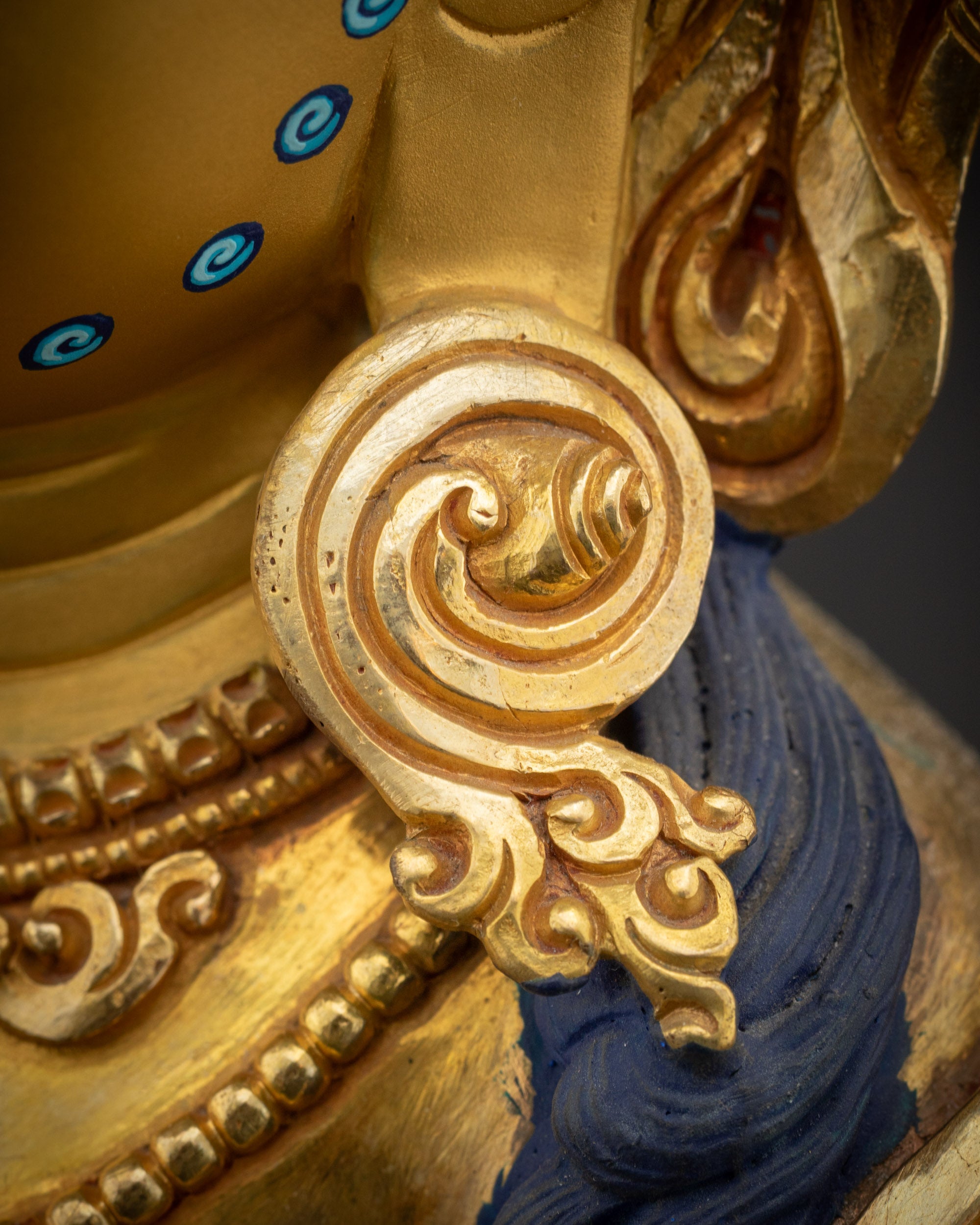 Close up of right side Earrings Dzambhala statue with carved folds and gold-gilded details