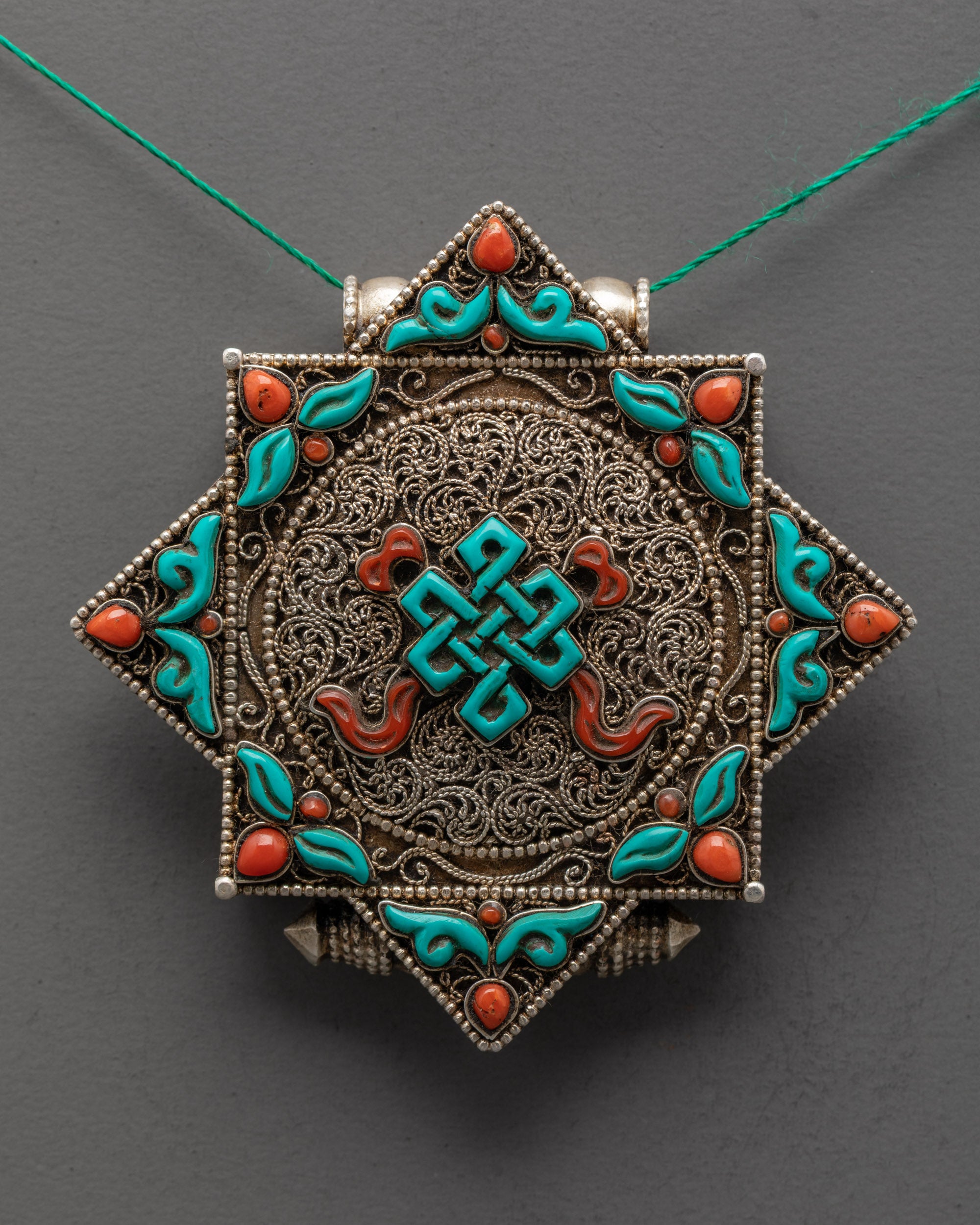 Close up of turquoise Endless Knot centerpiece on silver-plated filigree locket design
