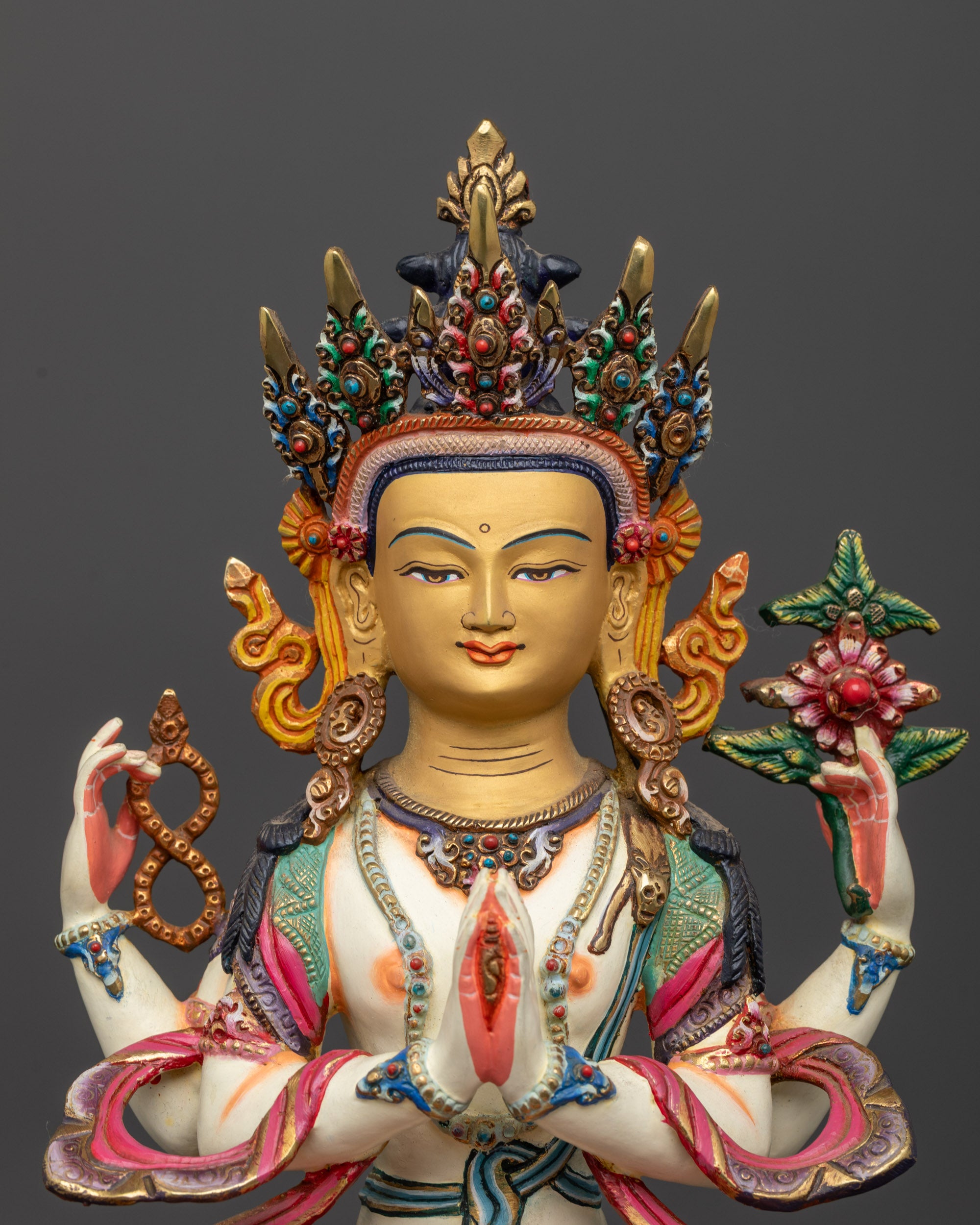 Close up on the four arms holding a lotus, rosary, and wish fulfilling gem.

