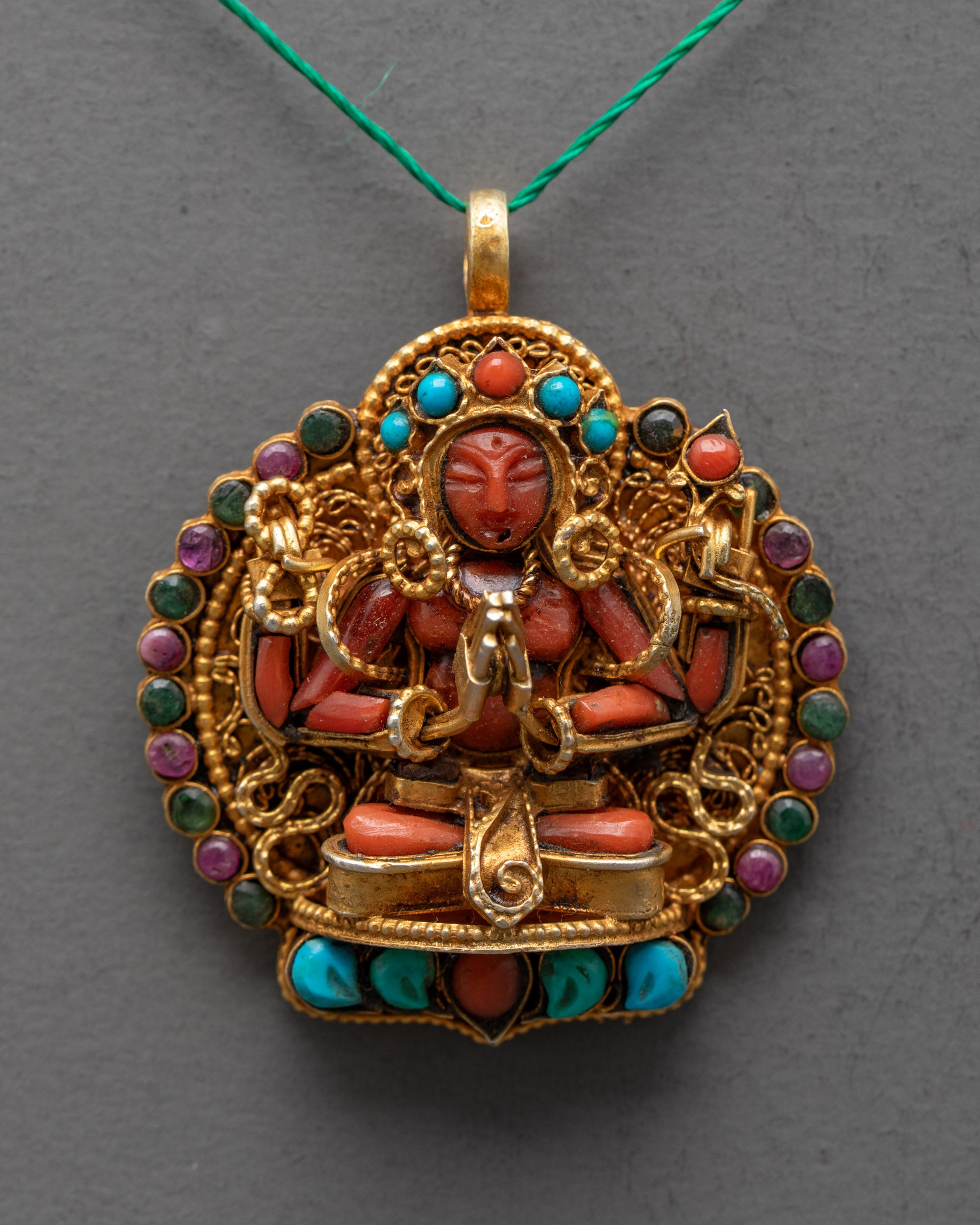 Closeup of Chenrezig Locket details showing red crystal deity, intricate filigree, and gemstone embellishments on a gold-gilded body.