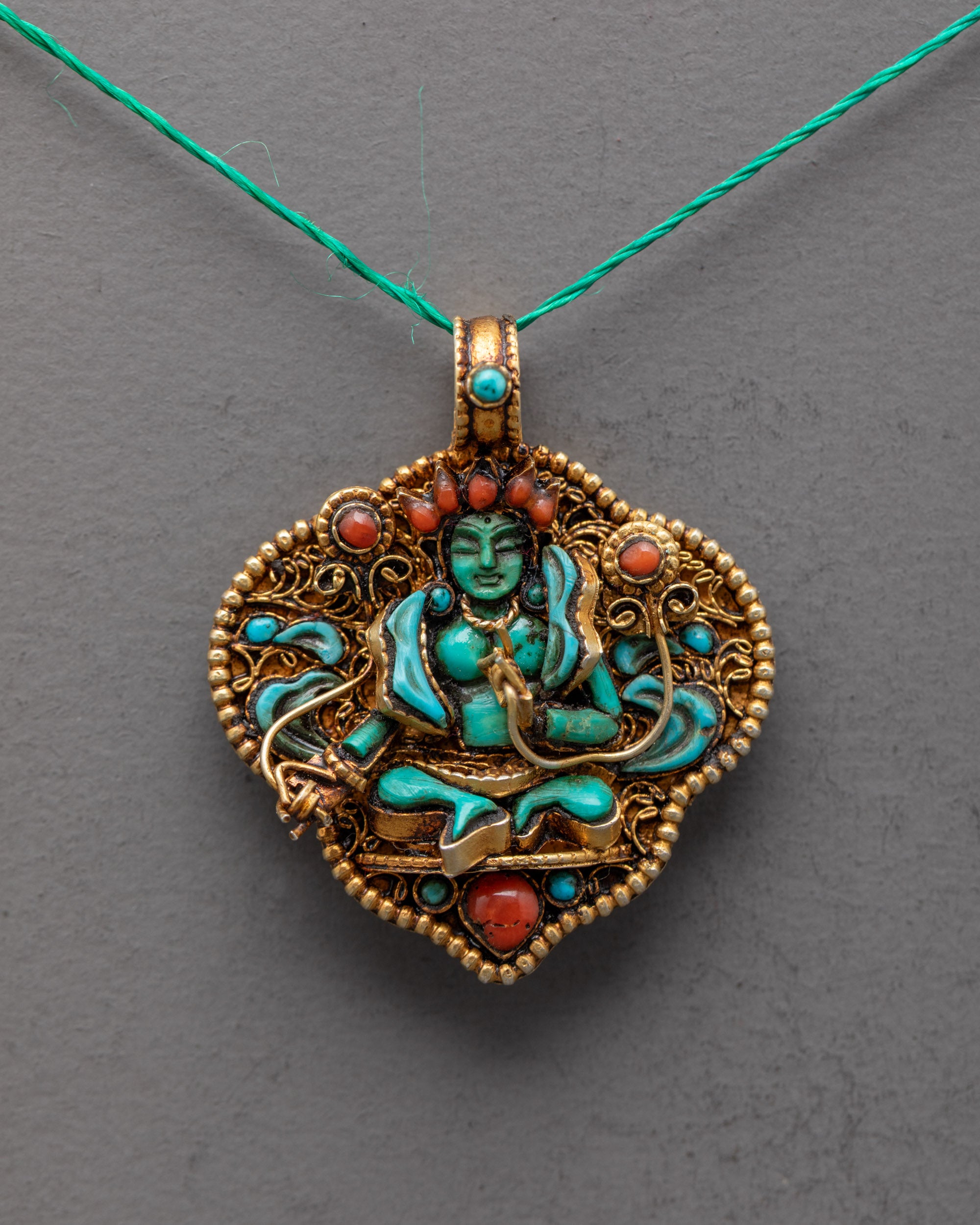 Closeup of Green Tara Amulet, showing intricate filigree work, radiant green crystal Tara, and detailed semi-precious stone inlays.
