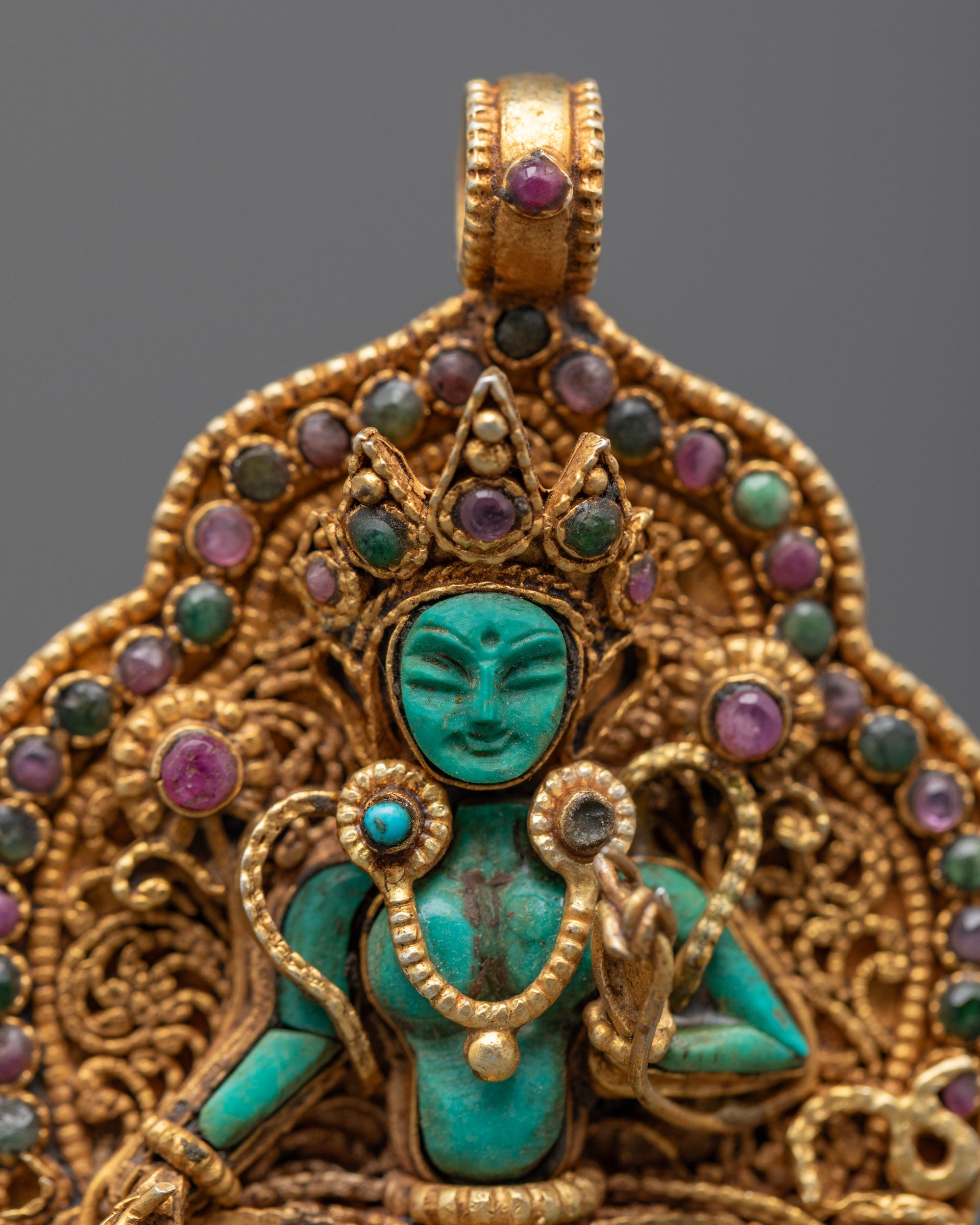 Closeup of Green Tara Locket showing detailed filigree work, green crystal deity, and semi-precious stones on a gold-gilded pendant.