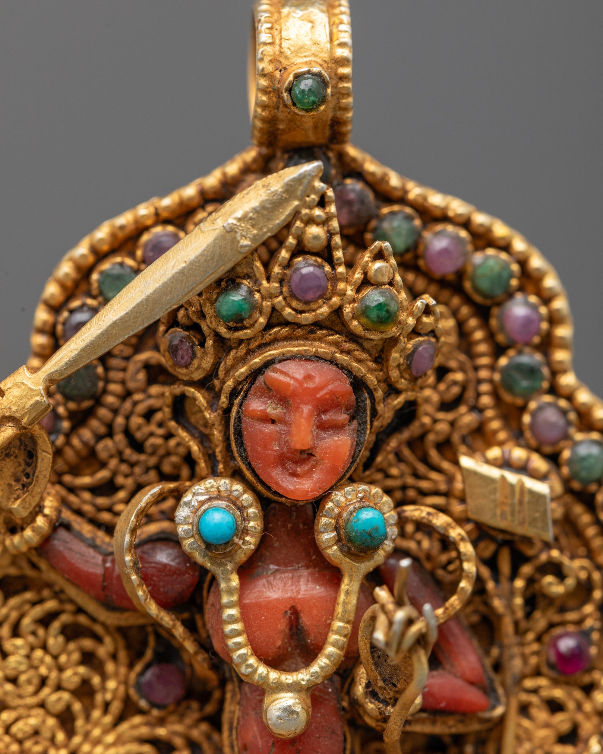 Closeup of Manjushri Locket showing intricate filigree, red crystal deity holding sword, and semi-precious stones on gold-gilded pendant.