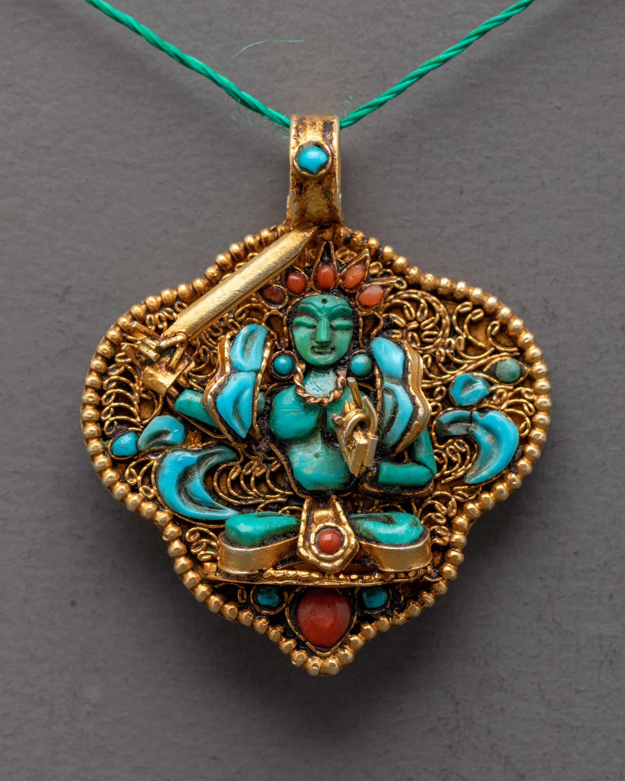 Closeup of Manjushri Locket showing intricate filigree work, green crystal deity, and semi-precious stones on a gold-gilded pendant.