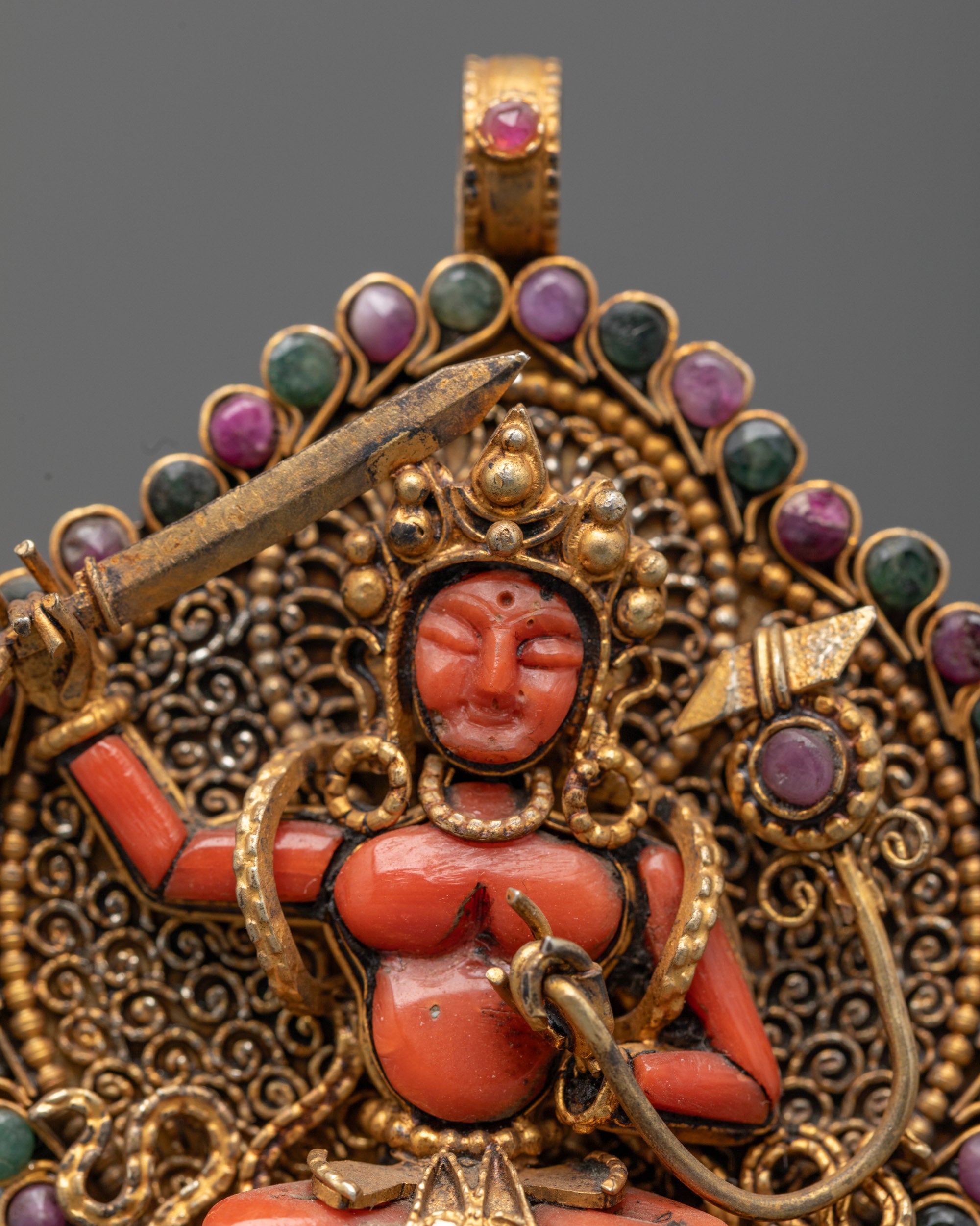 Closeup of Sacred Manjushri pendant showing coral figure and detailed gold filigree work