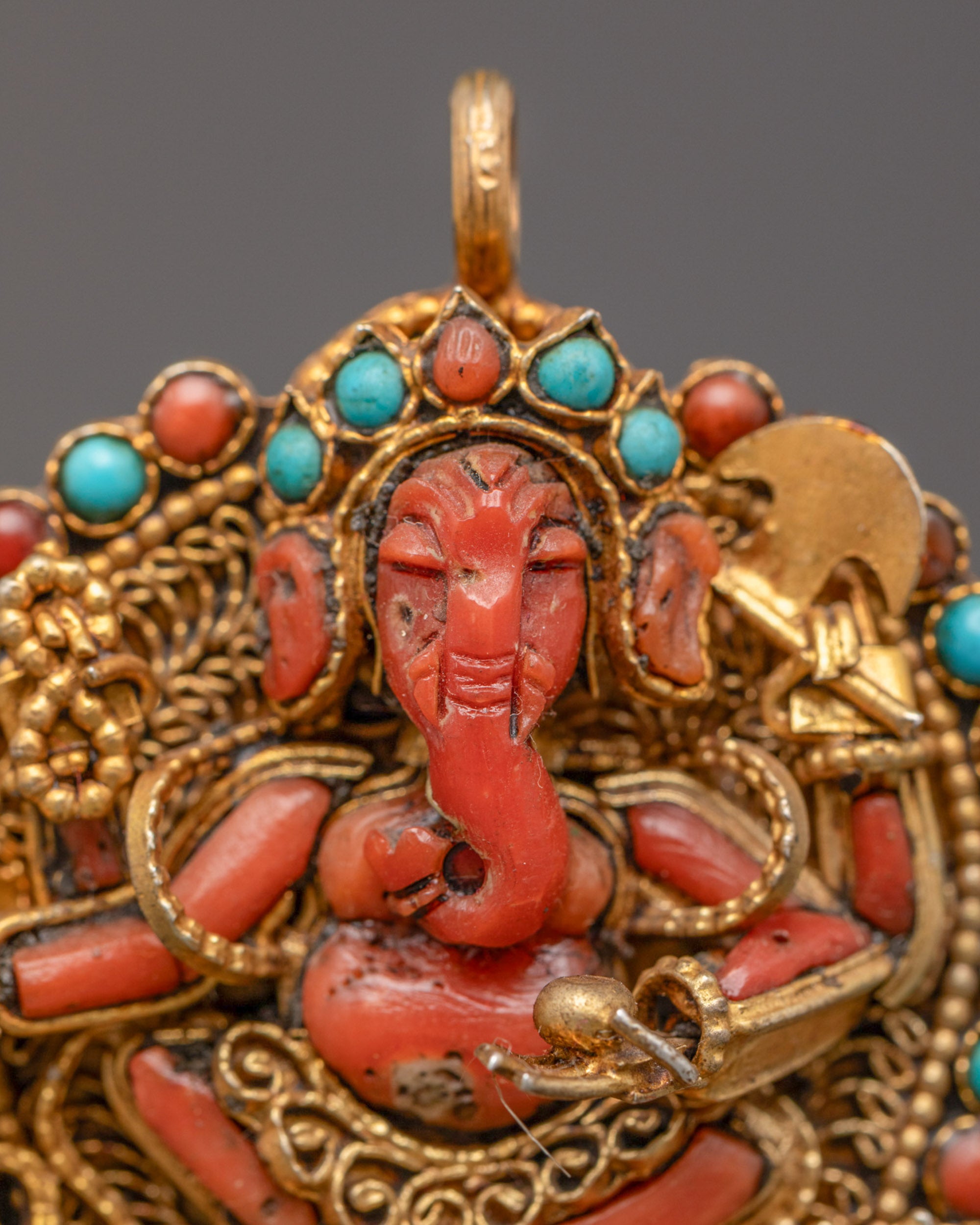 Closeup of handcrafted coral Ganesh pendant showing four-armed deity and detailed carving